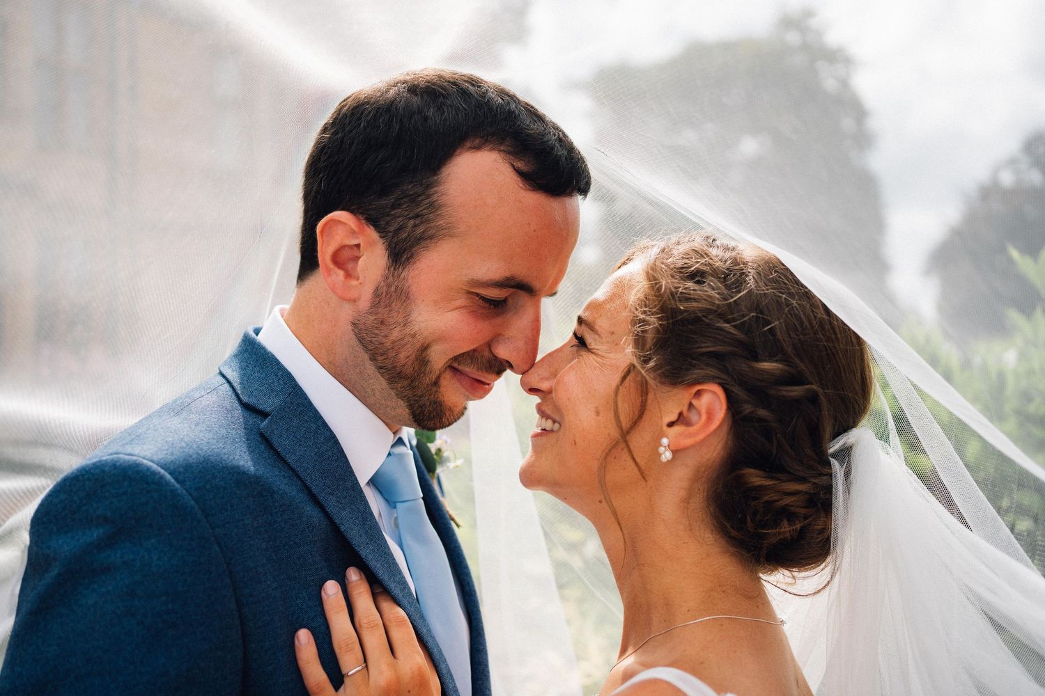 Romantic wedding couple shares intimate moment under flowing white veil.
