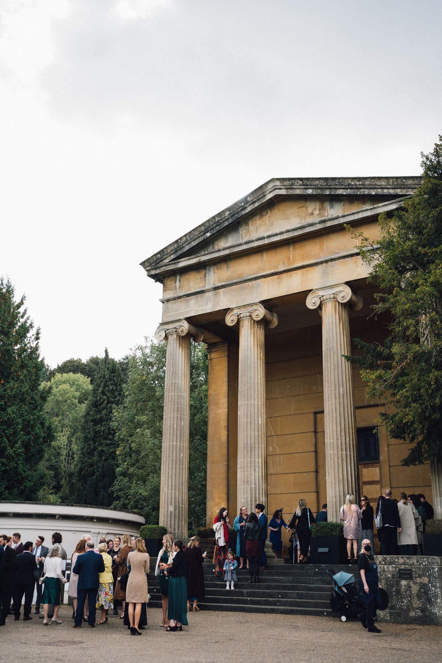 Wedding guests gather outside a historic neoclassical building with Ionic columns and stone steps.
