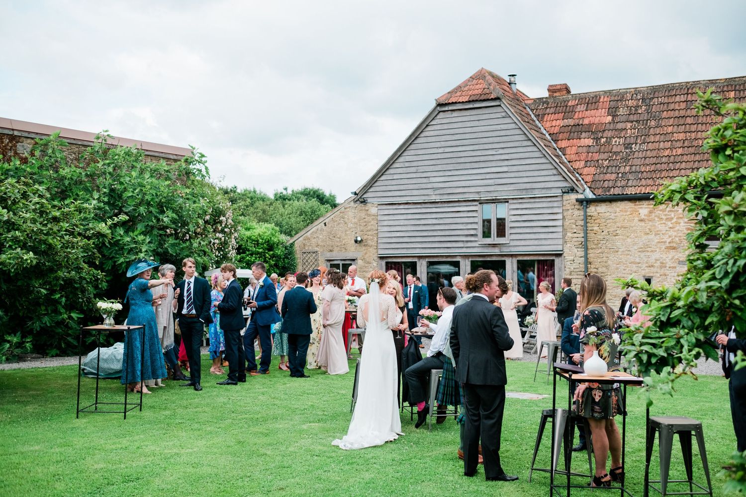 Wedding guests gather on a grassy lawn outside a rustic barn venue during an outdoor celebration.