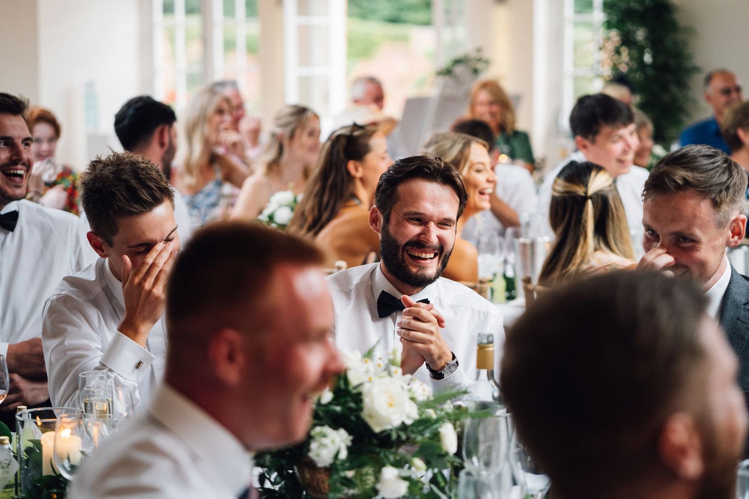 Wedding guests share joyful moments at reception dinner with white floral centerpieces.