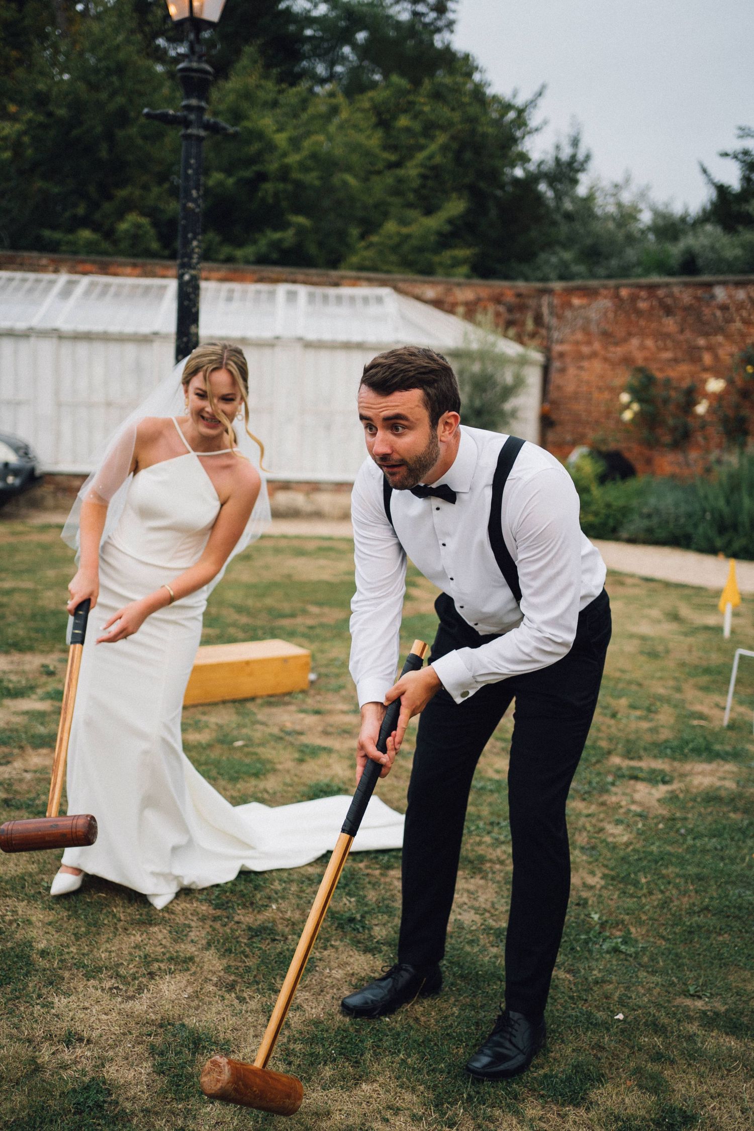 Wedding couple plays croquet on a lawn with vintage wooden mallets.