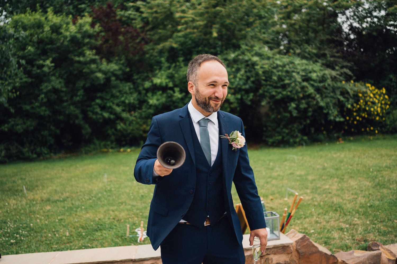 A person in a navy suit playing outdoor wedding games on a lawn.