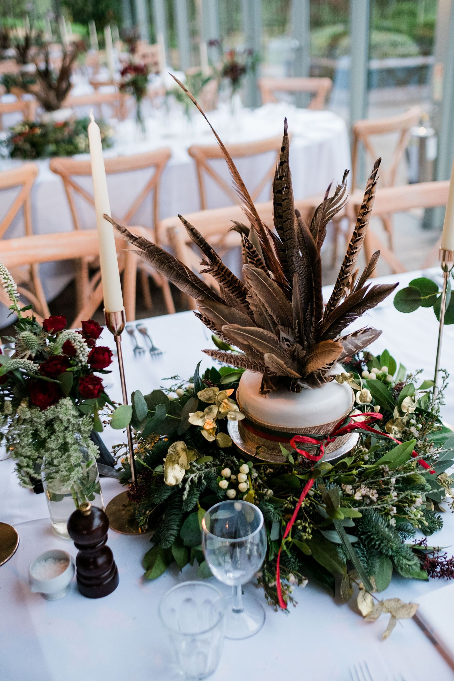 Elegant table settings with feather and floral centerpieces in rich burgundy and green tones.