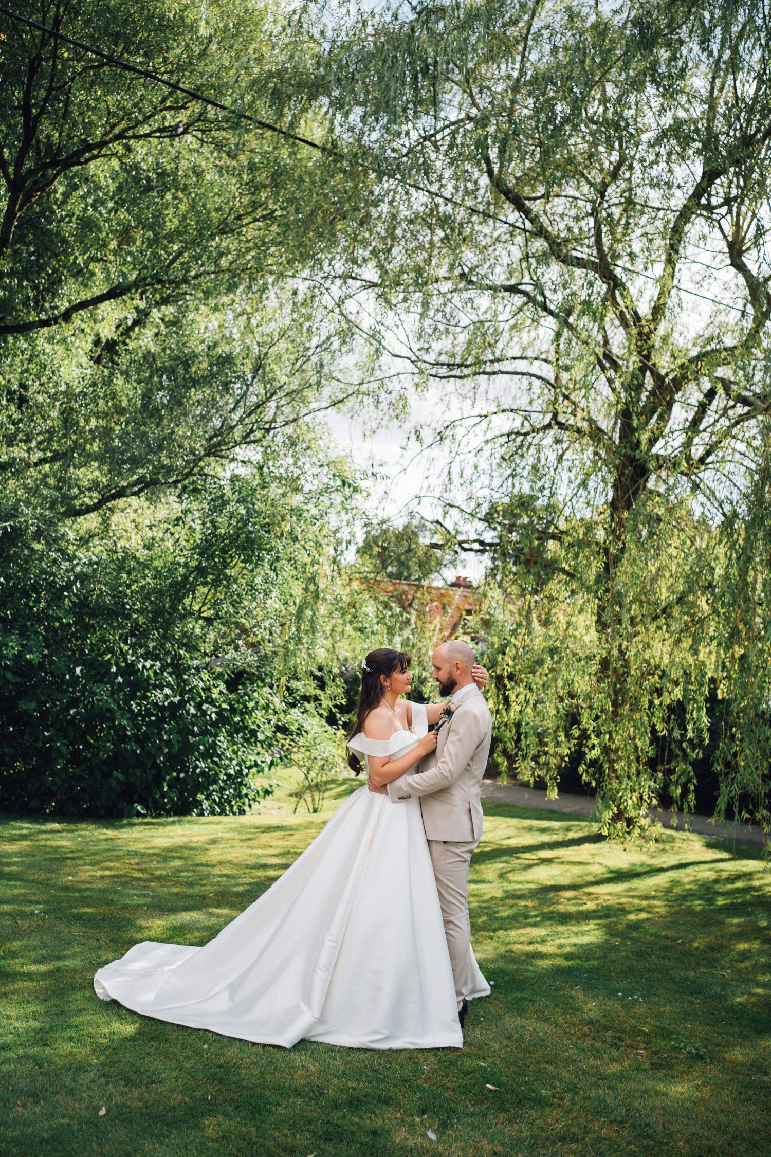 Wedding couple dances and spins on green lawn under weeping willow trees on sunny afternoon.