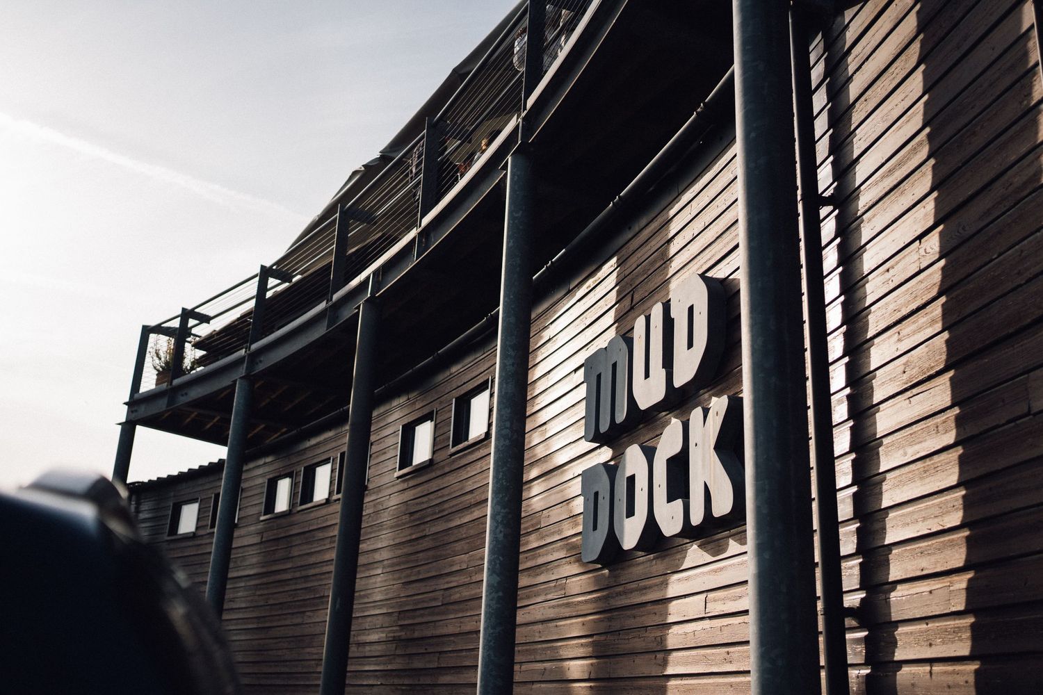 Mud Dock venue exterior featuring rustic wooden curved walls with bold signage against a clear sky.