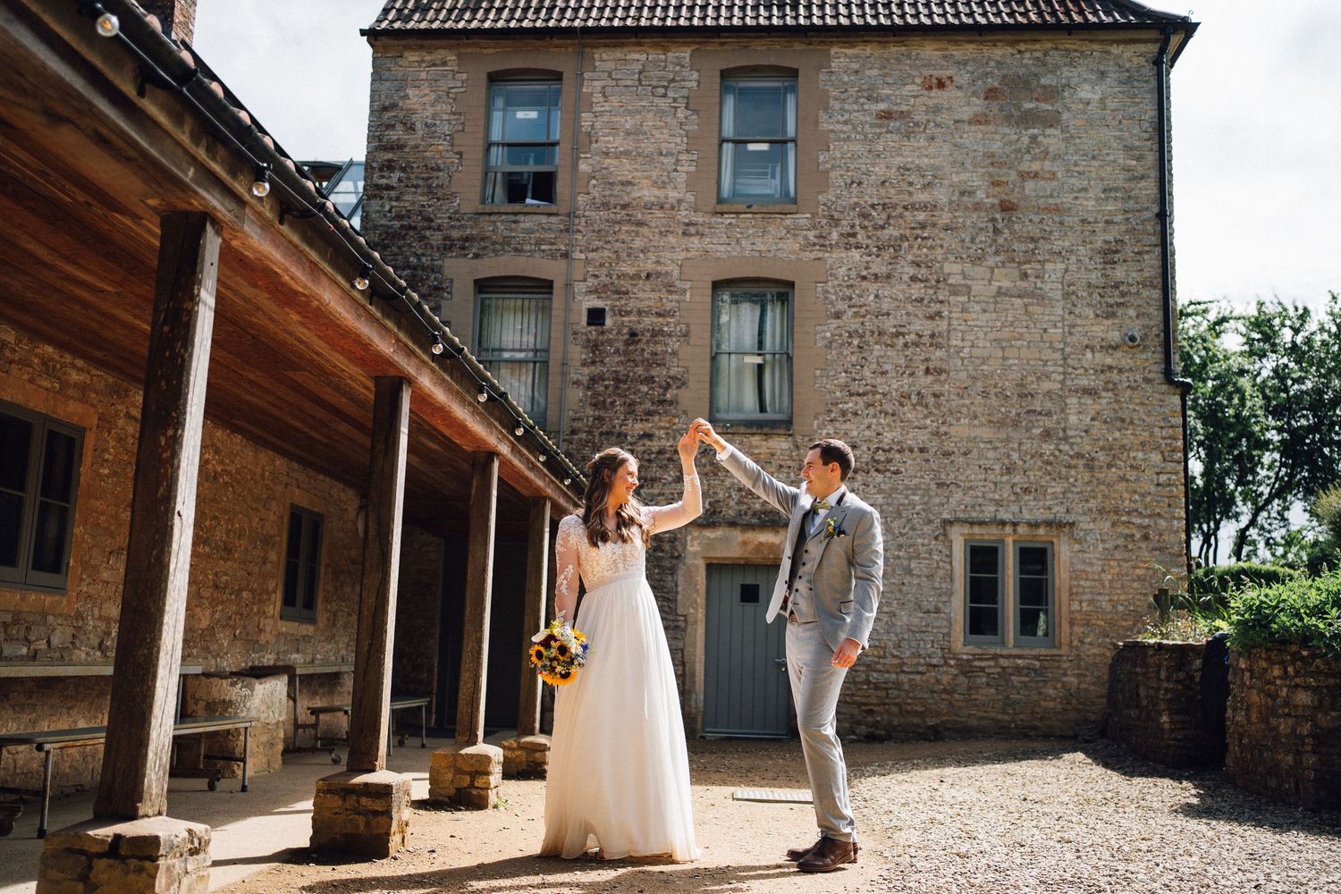 Bride and groom dancing outdoors at a rustic stone building wedding venue on a sunny day.