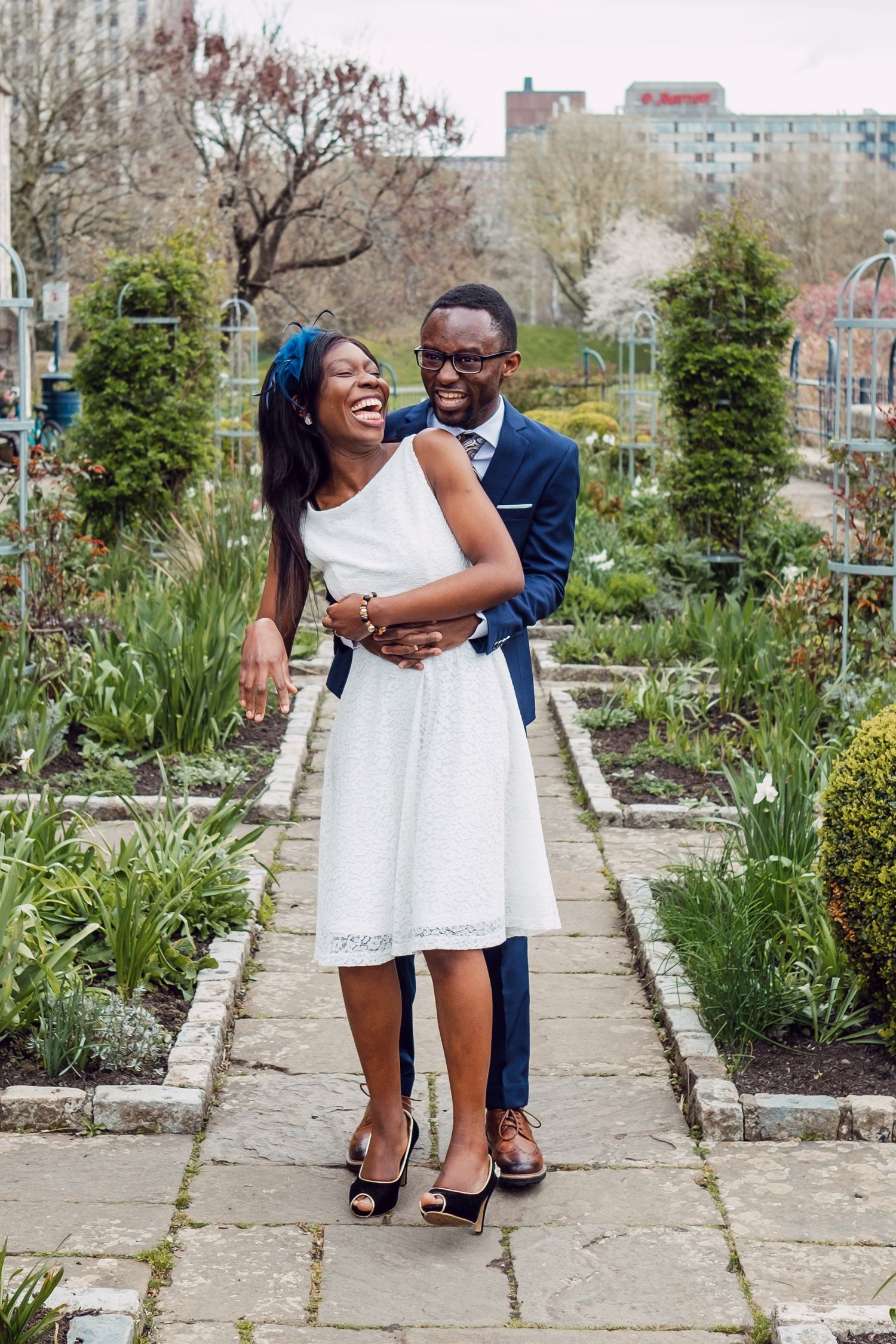 A couple laughs together while posing in an outdoor garden setting.