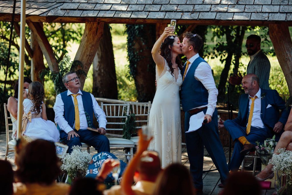 Wedding guests celebrate during an outdoor garden reception under a tent with string lights.
