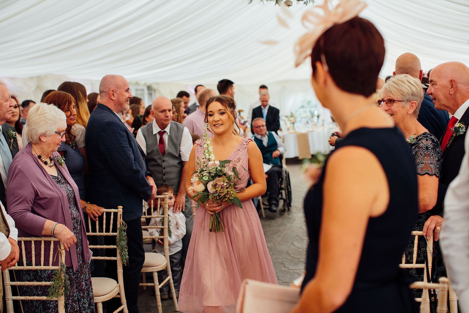 Wedding ceremony guests seated in rows under an elegant white tent canopy.
