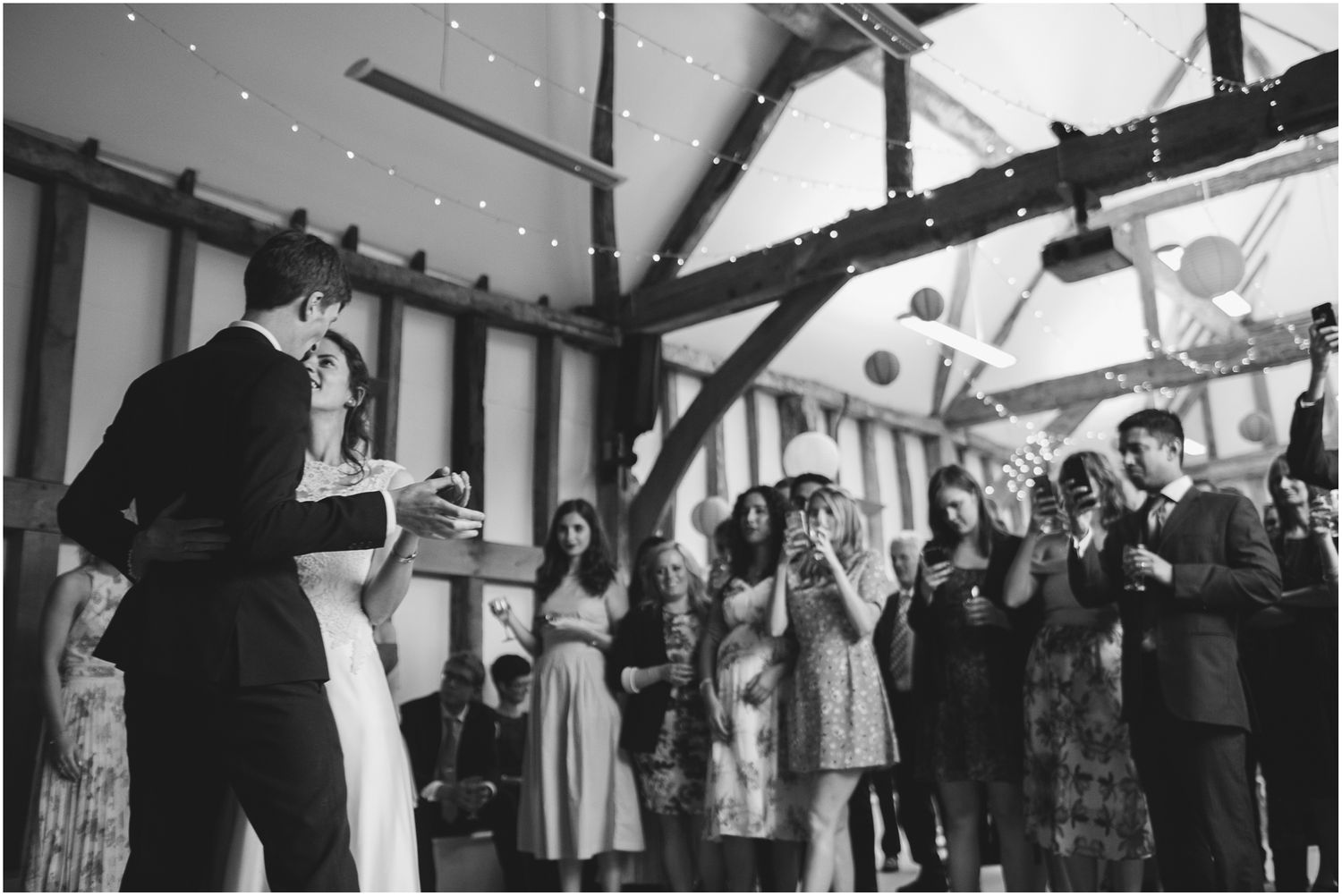 Wedding guests dancing beneath twinkling string lights in a rustic barn venue.