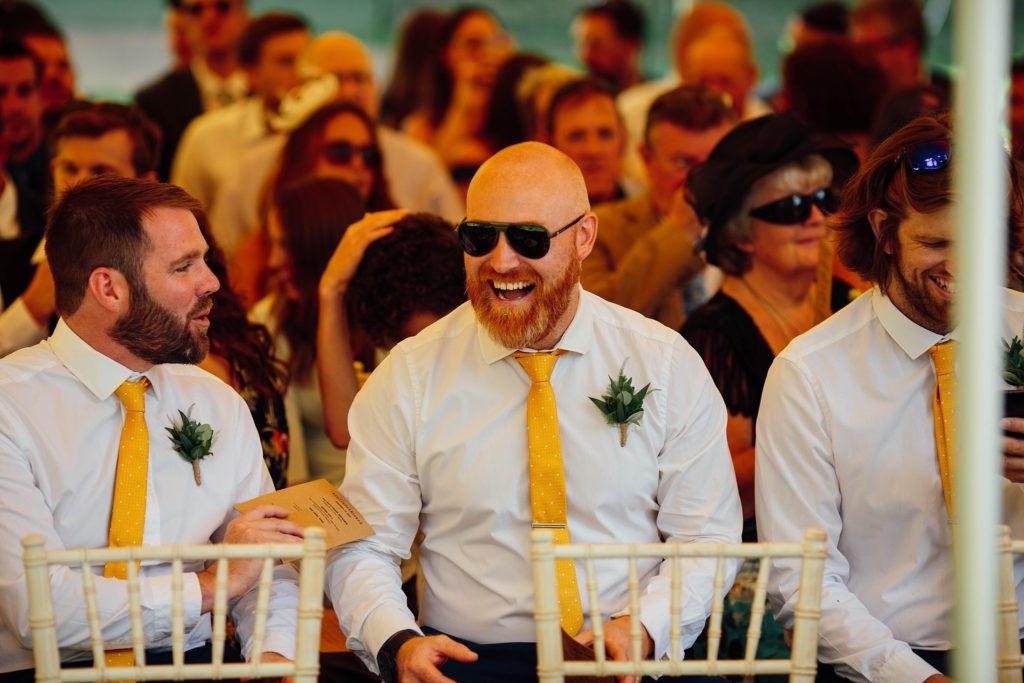 Wedding celebration with guests in white shirts and yellow ties under tent.