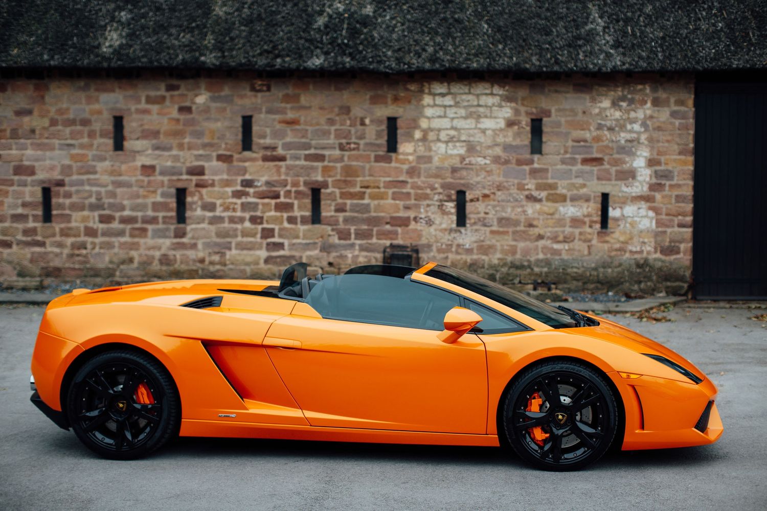 An orange Lamborghini Gallardo sports car parked against a brick wall background.