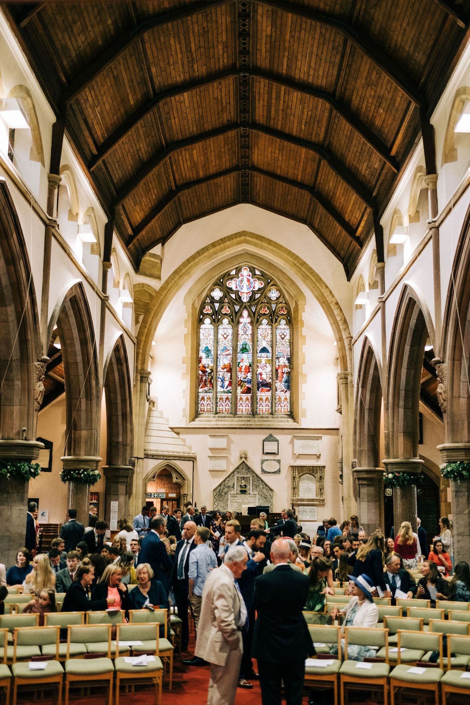 Interior of a Gothic church with vaulted ceilings and stained glass windows filled with wedding guests.