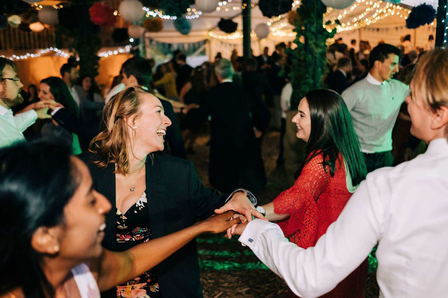 People dancing and celebrating at a lively wedding reception with warm ambient lighting.