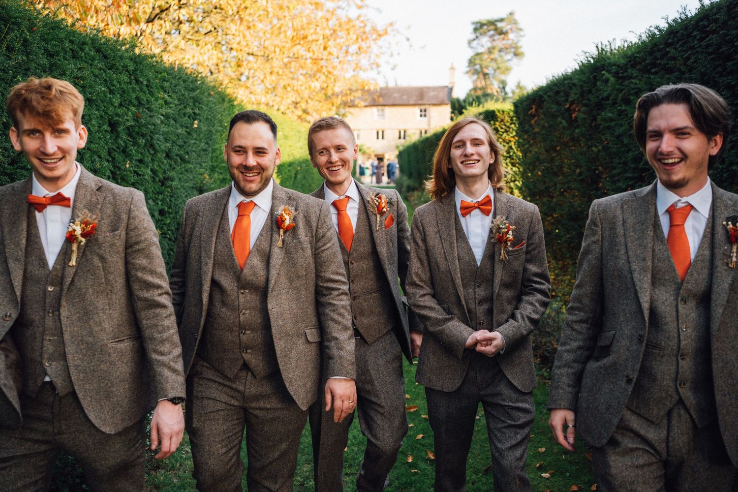 Wedding party in matching brown suits and orange ties smile for casual outdoor photo.
