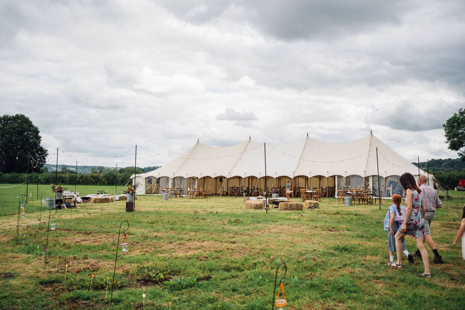 A large white wedding tent set up in a scenic countryside field with wooden chairs arranged outside.