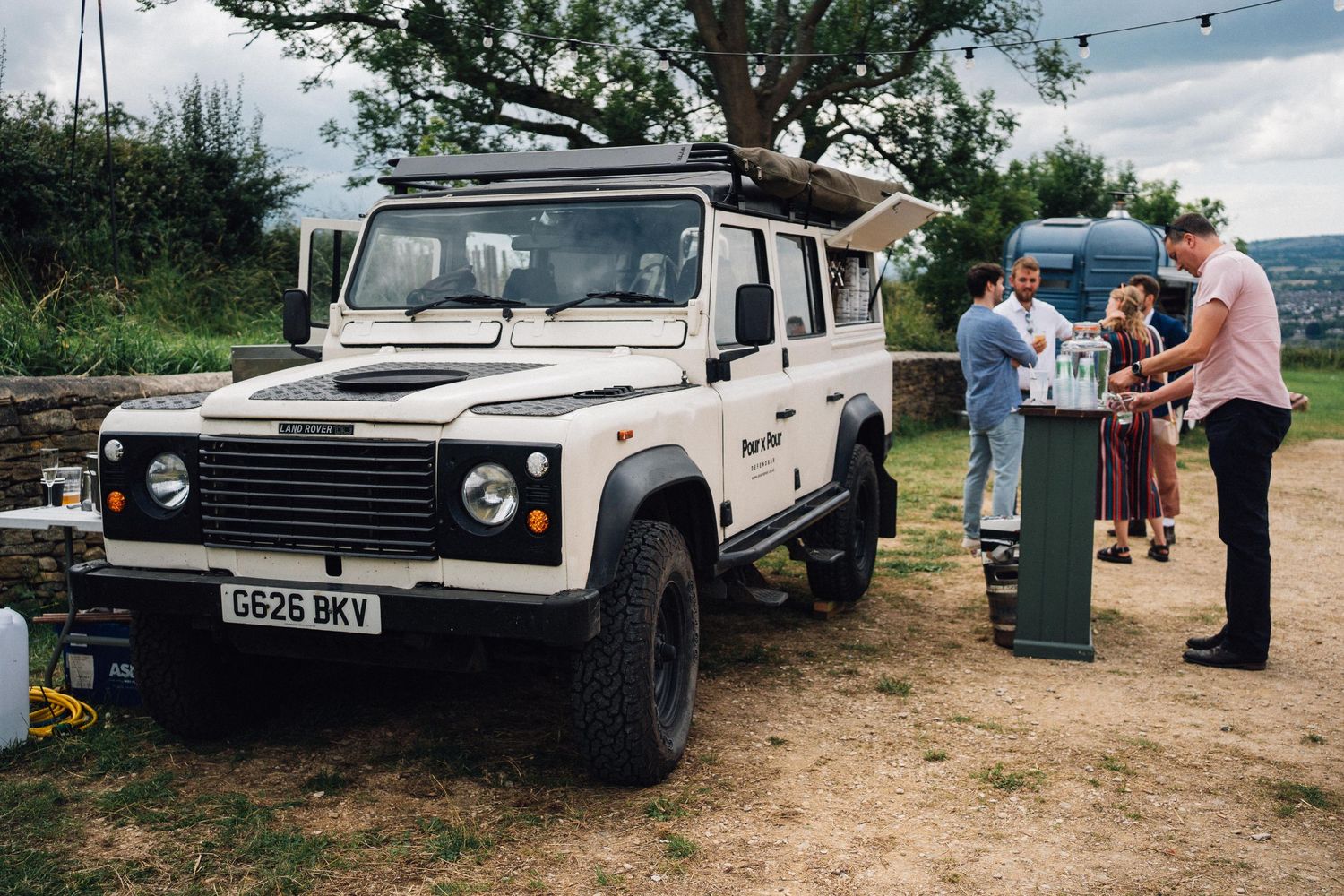 White Land Rover Defender parked at outdoor event with people gathered nearby.