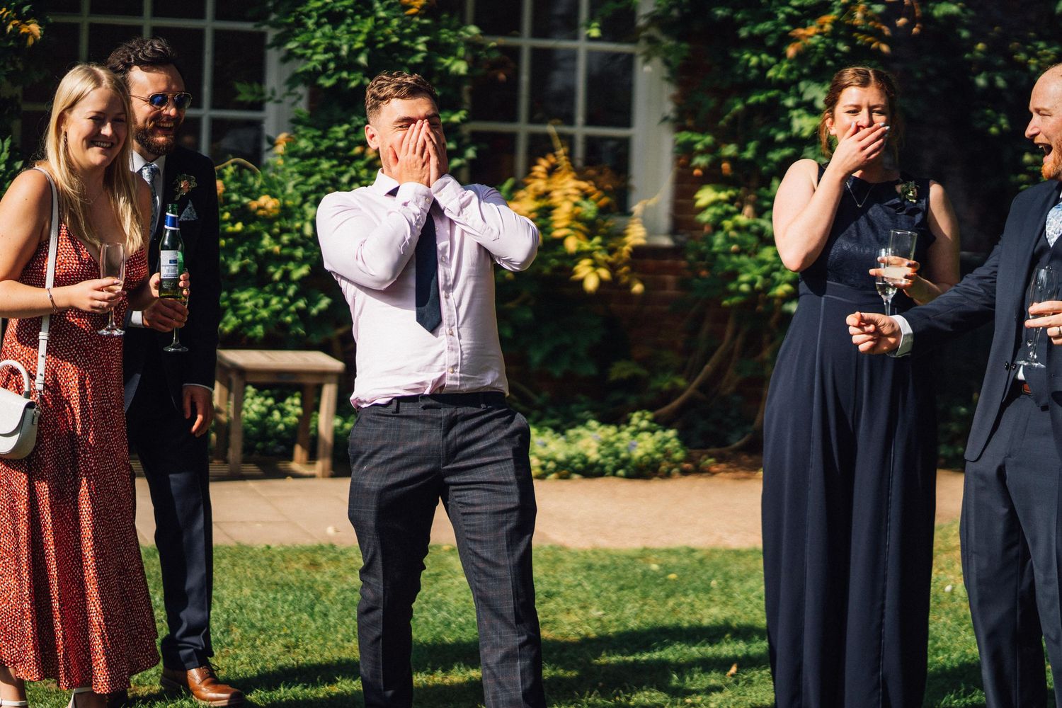 Wedding party members pose for photos in a sunny garden with yellow flowers.