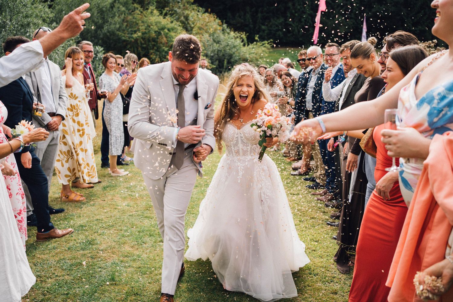 Joyful couple runs through a crowd of cheering wedding guests throwing confetti.