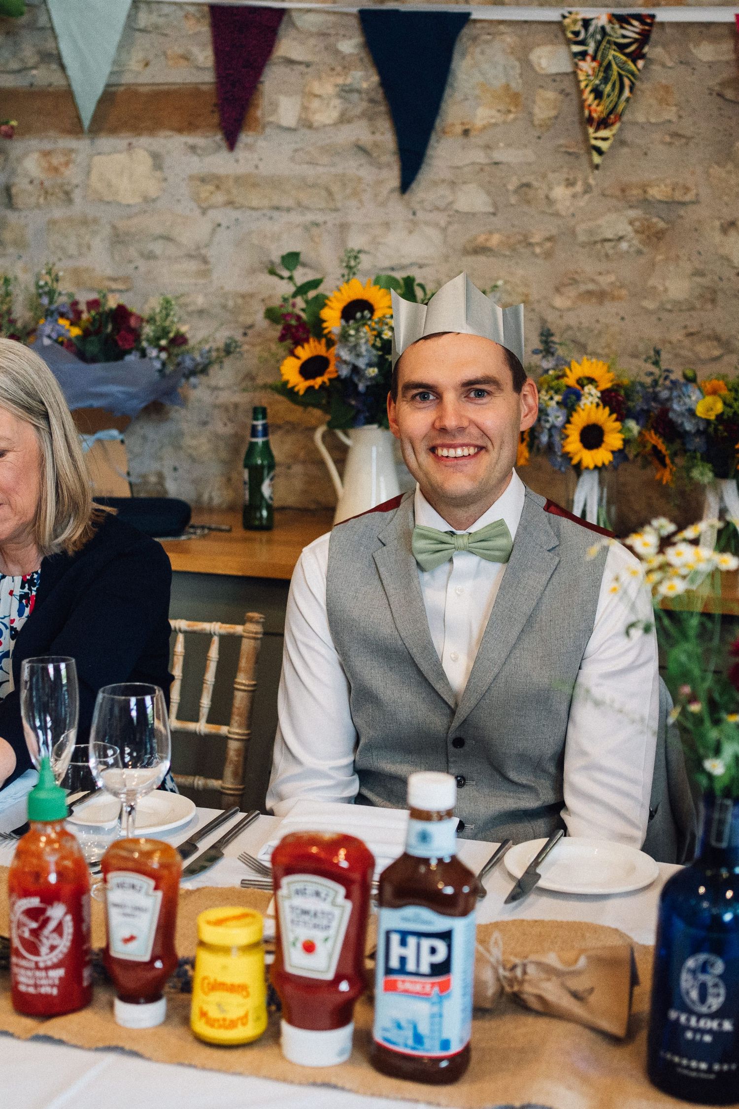 Wedding reception table with condiments and sunflower decorations against rustic stone wall.