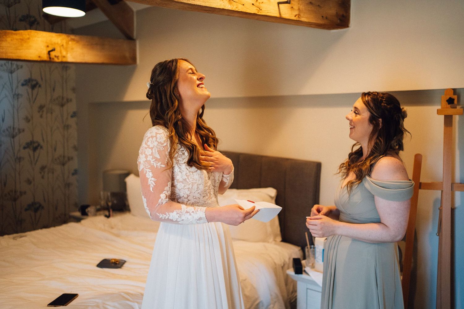 Wedding party members share laughs in a cozy room with wooden beam ceiling.