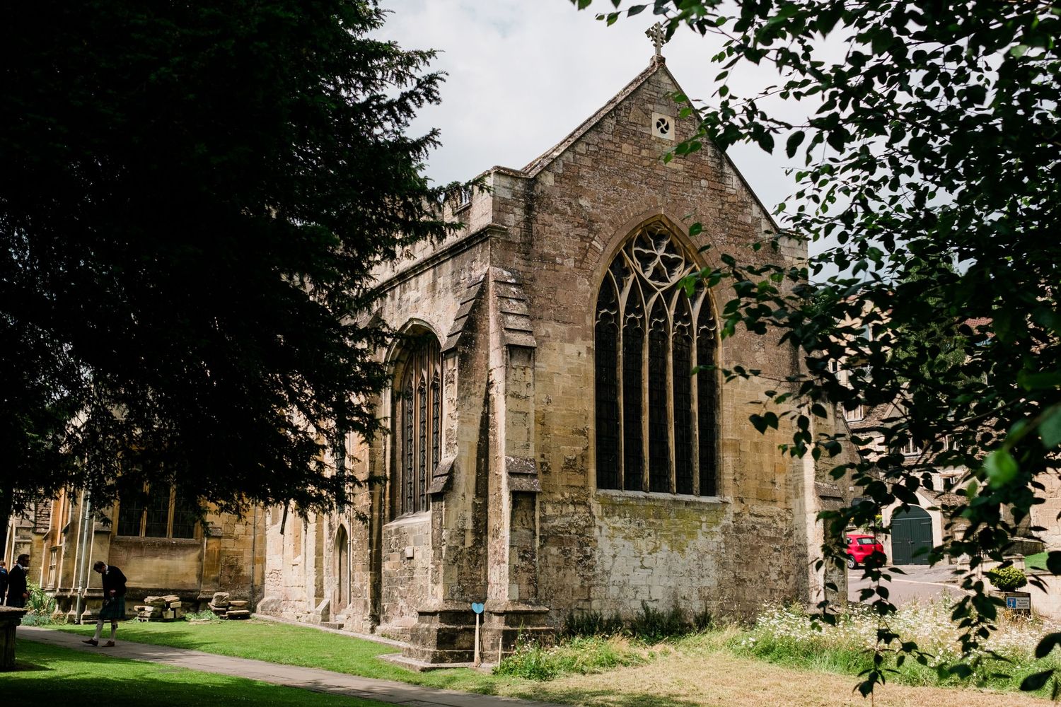 Historic stone church exterior with gothic windows surrounded by green trees.