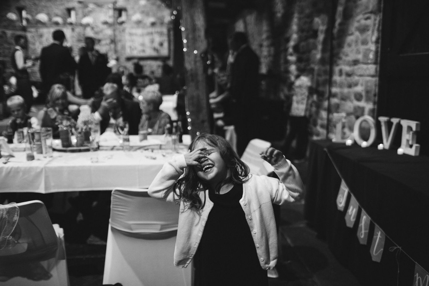 Black and white photo of a rustic wedding reception venue with exposed wooden beams and stone walls.