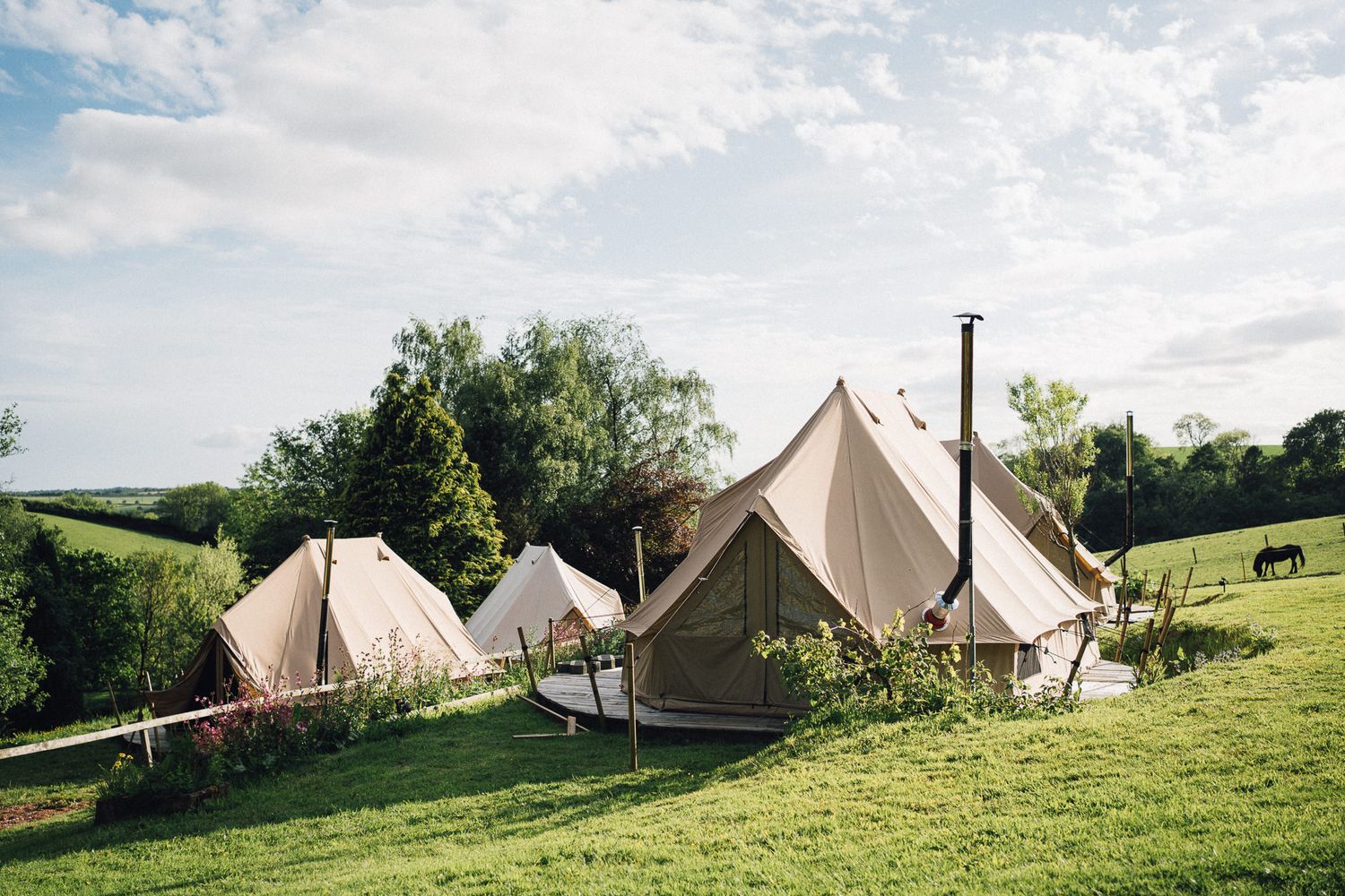 Row of luxury glamping tents arranged on a hillside under blue summer skies.