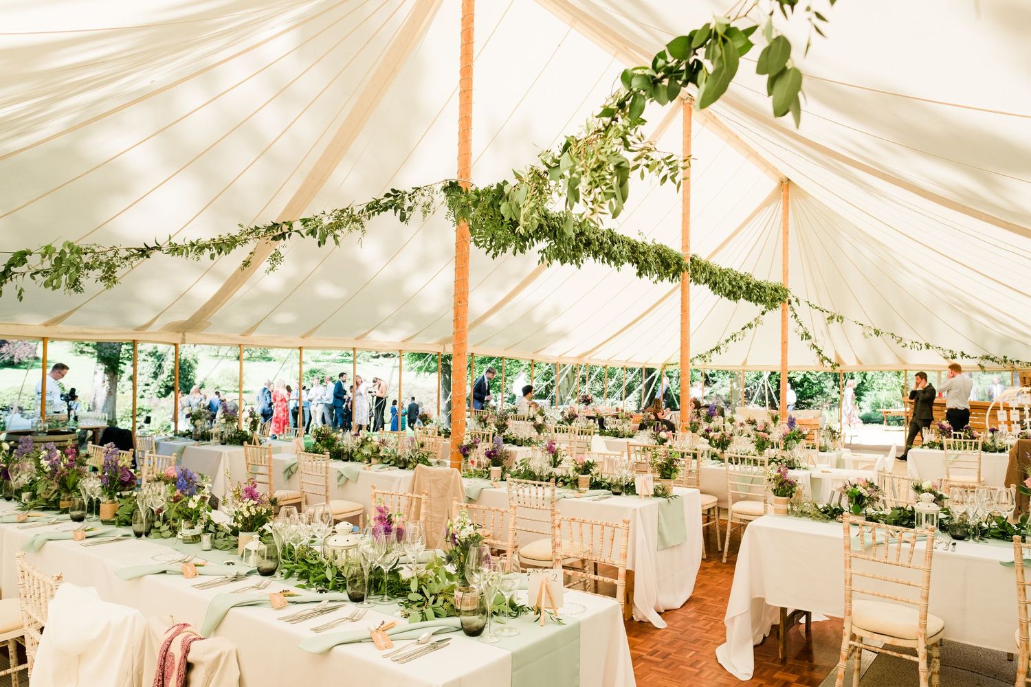 Elegant white wedding tent decorated with greenery garlands and draped fabric ceiling.
