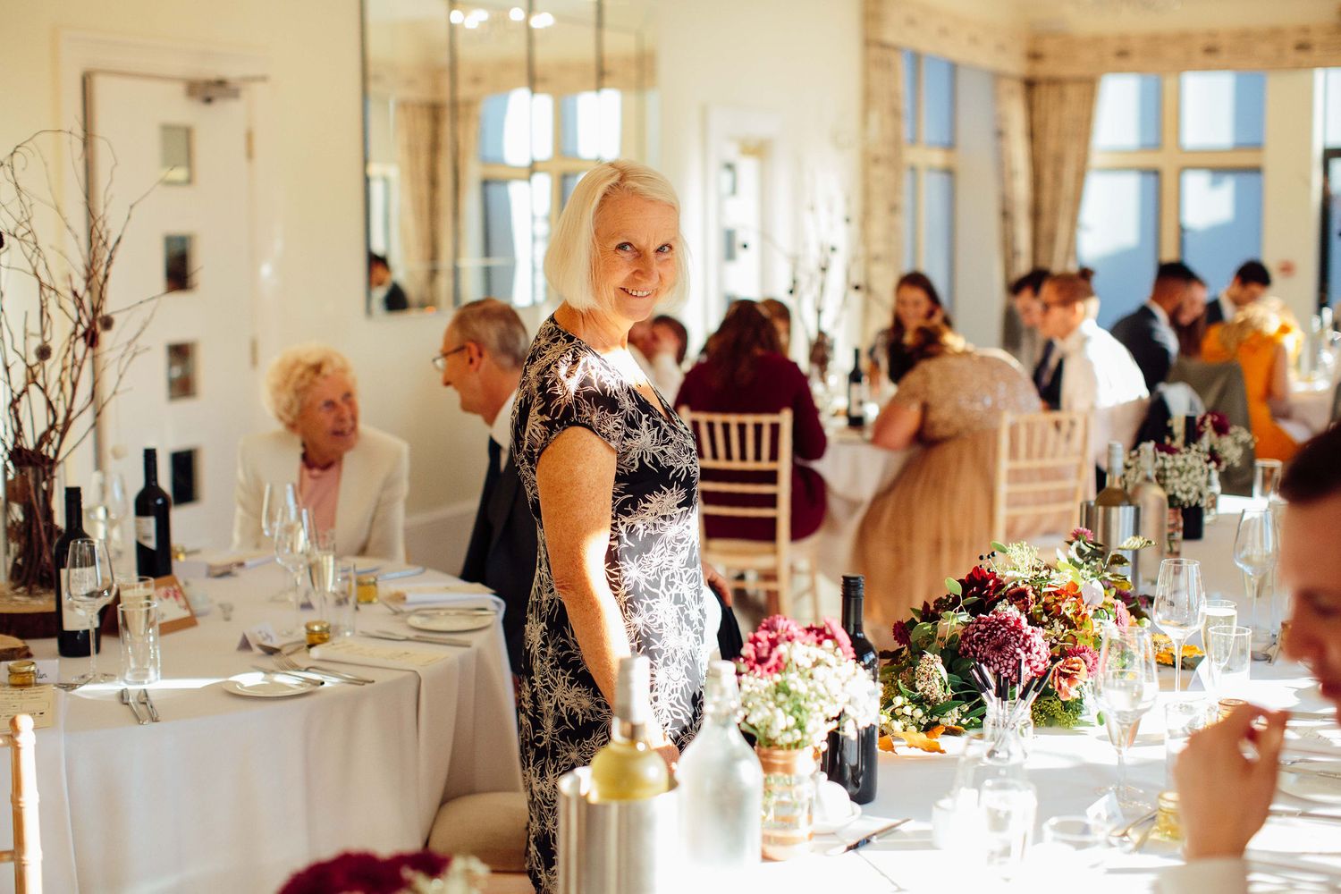 Bright reception hall with elegant table settings and guests mingling in formal attire.