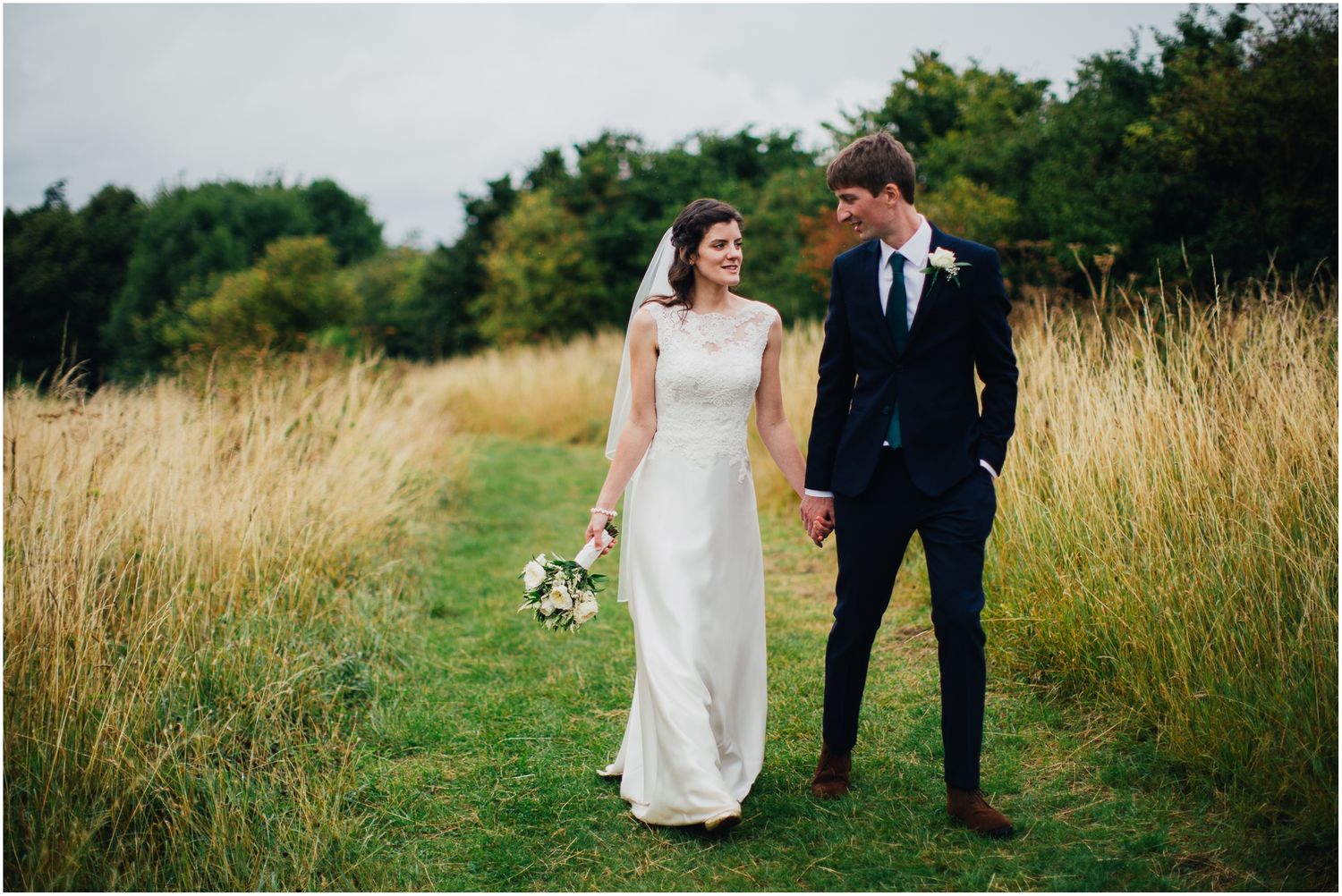 Couple walking through golden wheat field during sunset wedding photoshoot in countryside setting.