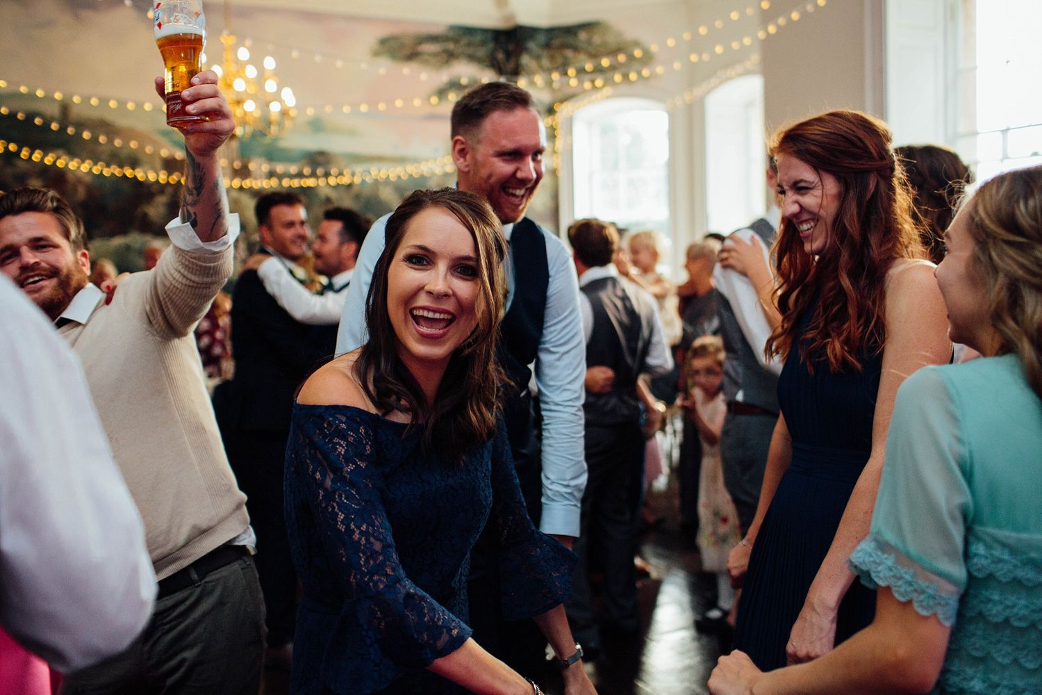 Lively wedding party dancing and celebrating in an elegant indoor venue with string lights.