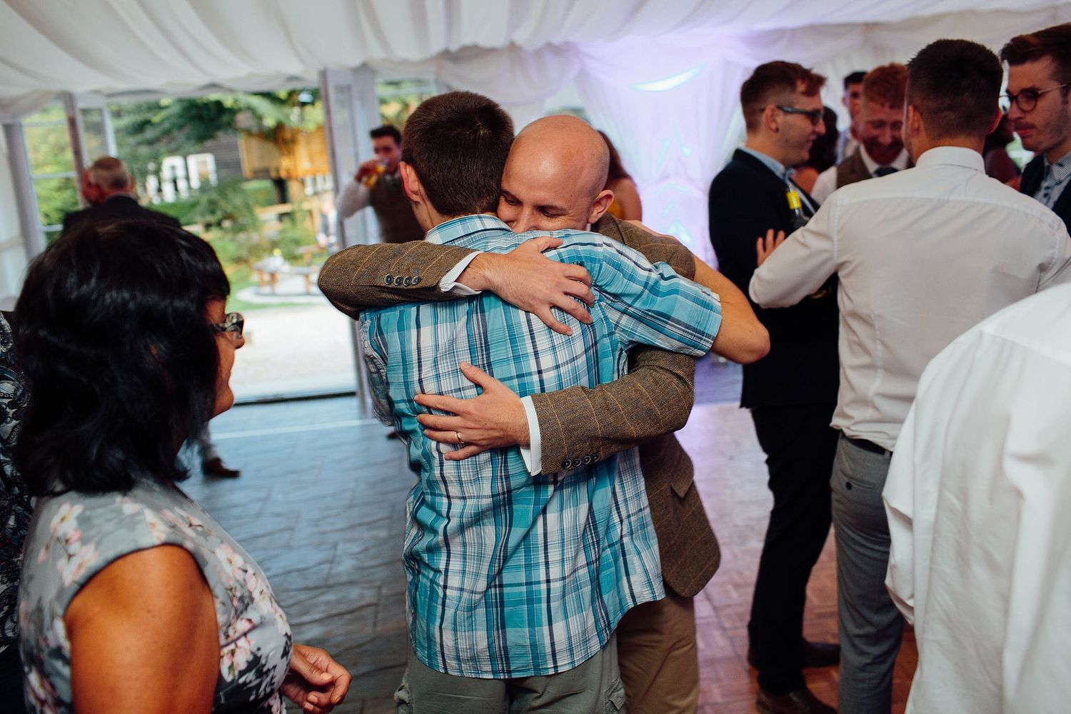 Emotional guests share warm embraces during a heartfelt moment at a wedding reception.