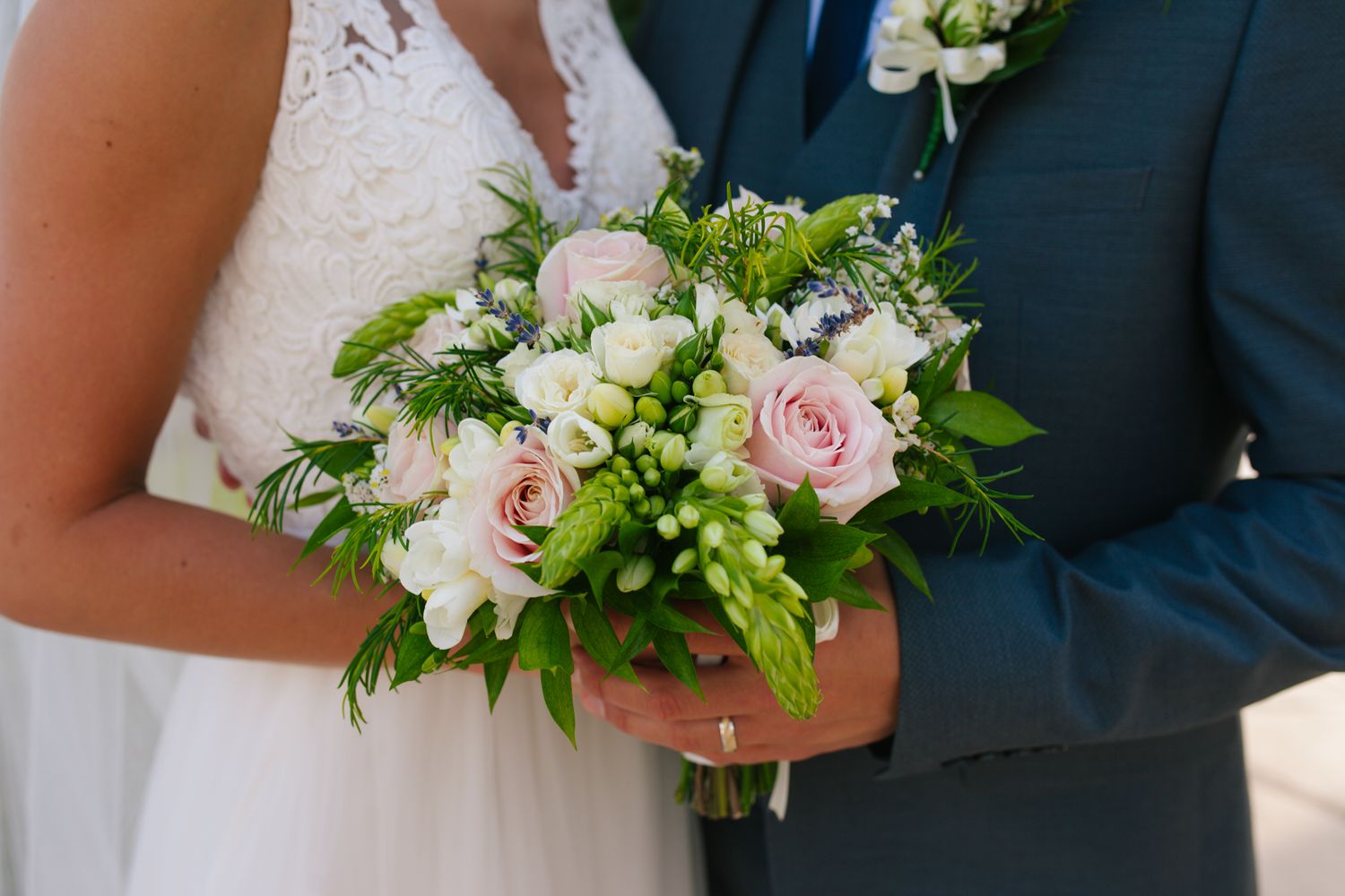 A delicate bridal bouquet featuring pink roses, white flowers and green foliage held against formal attire.