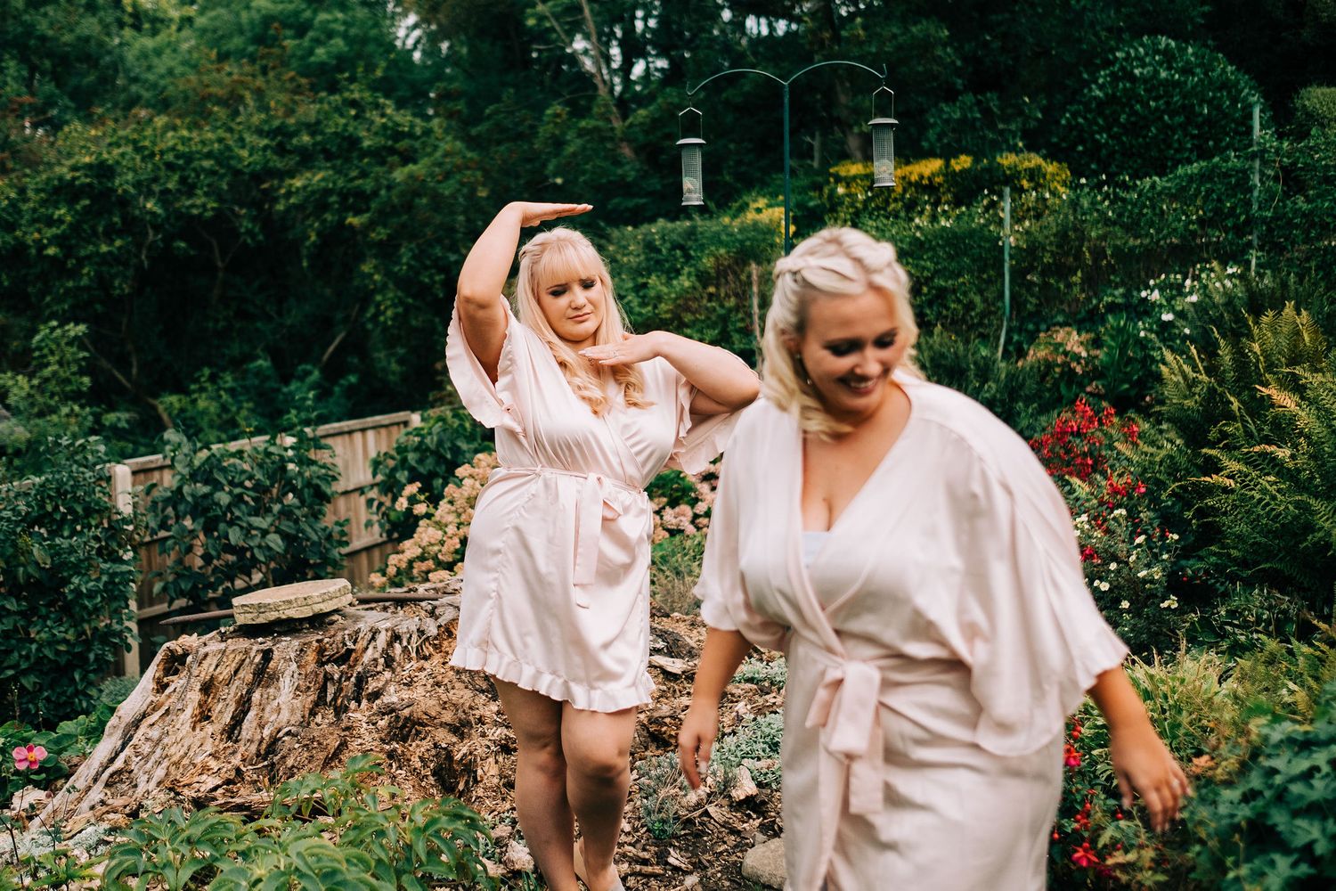 Group wearing light colored dresses walking together in a lush garden setting.