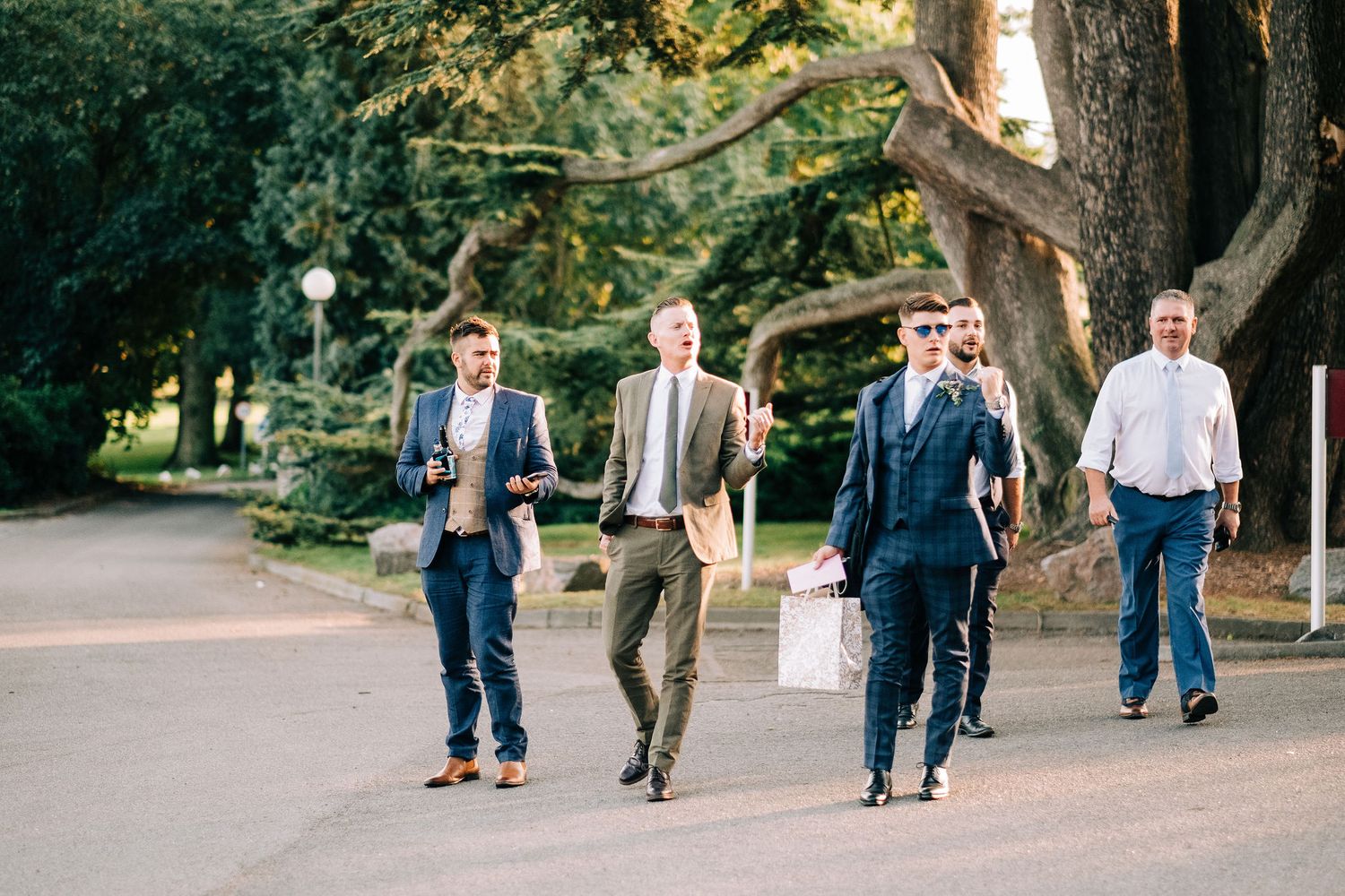 Wedding party walking along garden path outside historic venue at sunset.
