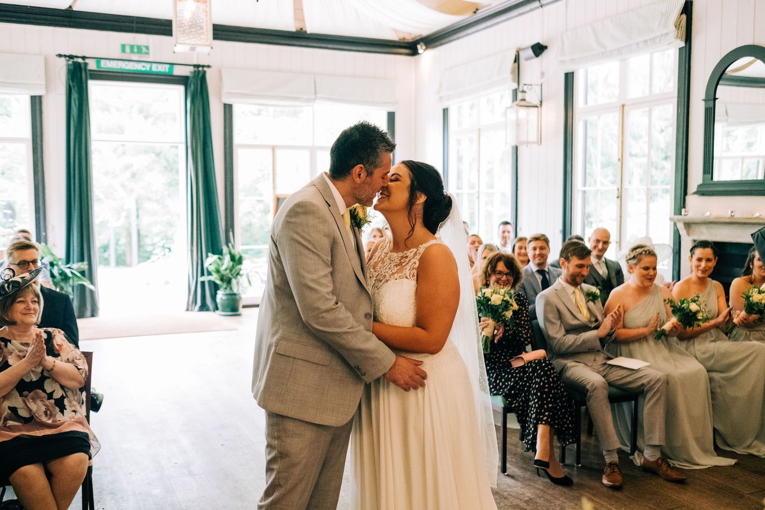 Elegant indoor wedding venue with white drapes and green accents during ceremony.