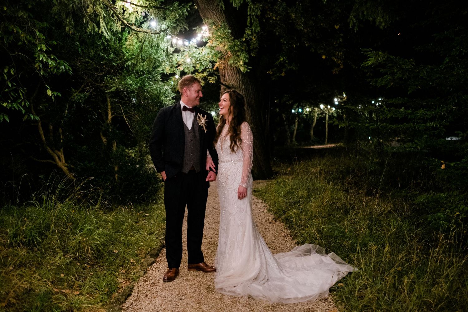 Romantic nighttime wedding portraits under illuminated trees.