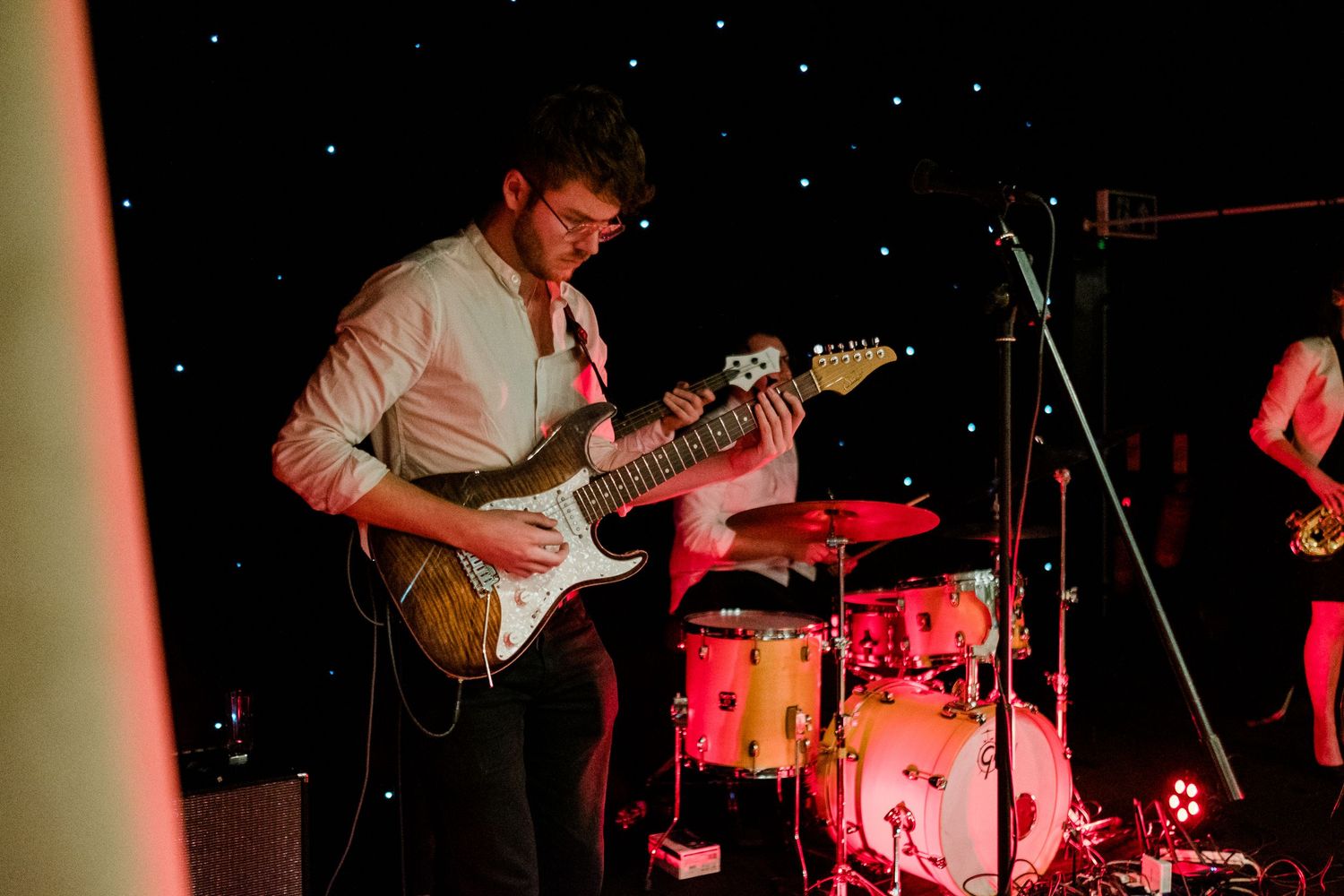 Musicians playing instruments on a darkened stage with red theatrical lighting.