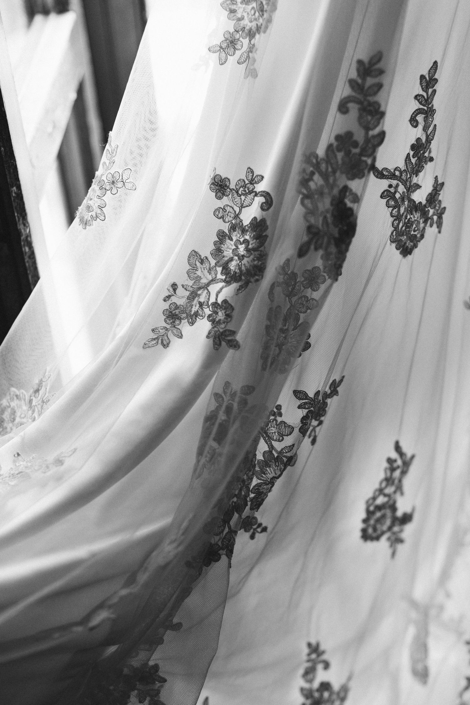 Black and white detail shot of intricate lace patterns on flowing wedding dress fabric.