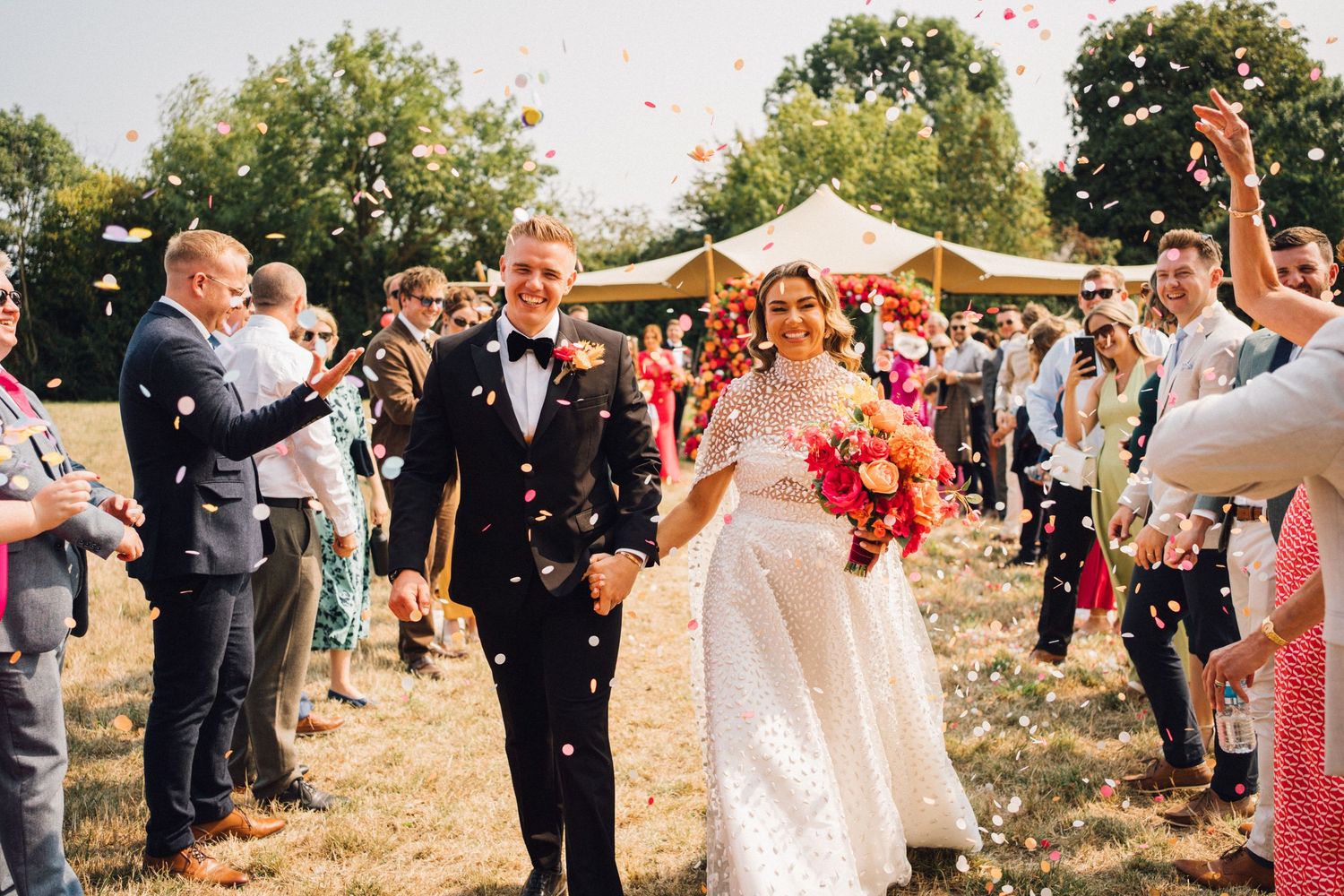 Wedding party and guests celebrating with confetti in a sun-filled outdoor ceremony.