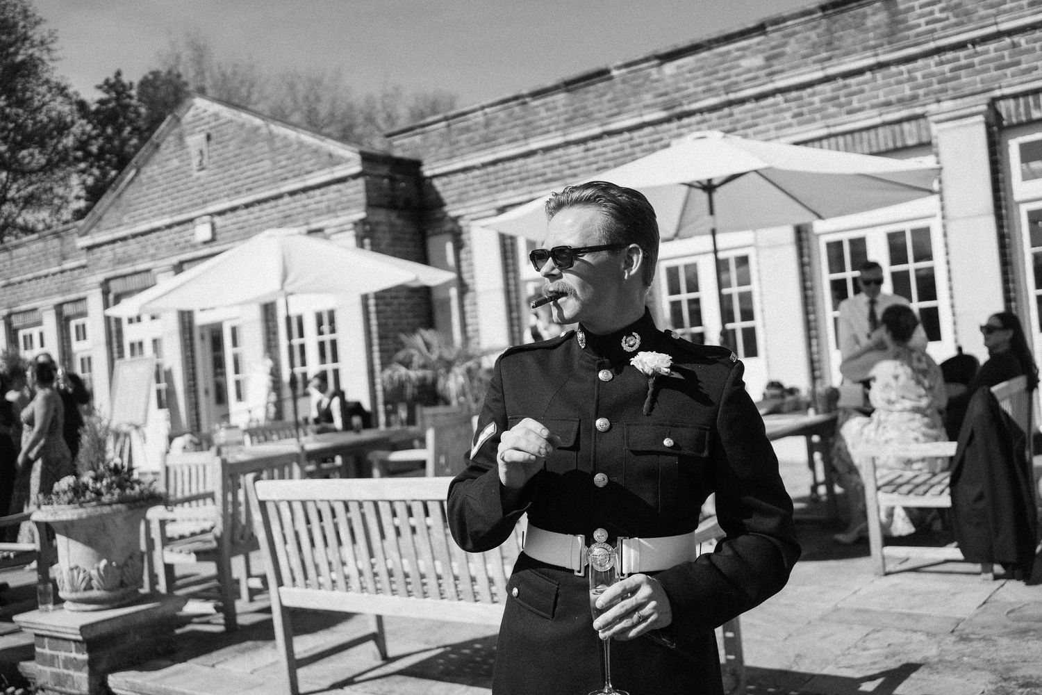 Man in military uniform smoking cigar outdoors at elegant venue on sunny day, black and white photo.