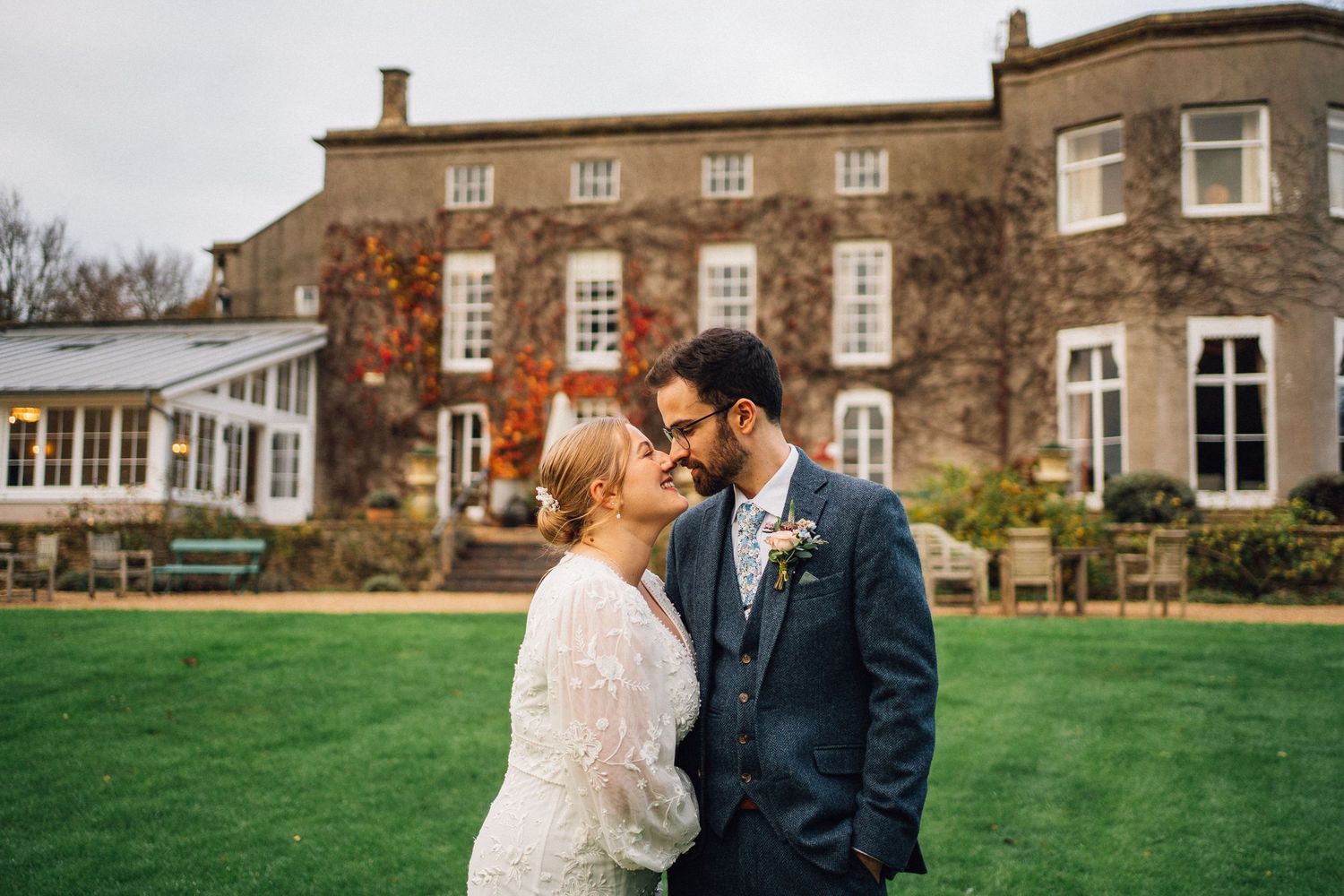 A romantic couple shares tender moments on the grounds of a historic stone manor house during an autumn wedding celebration.