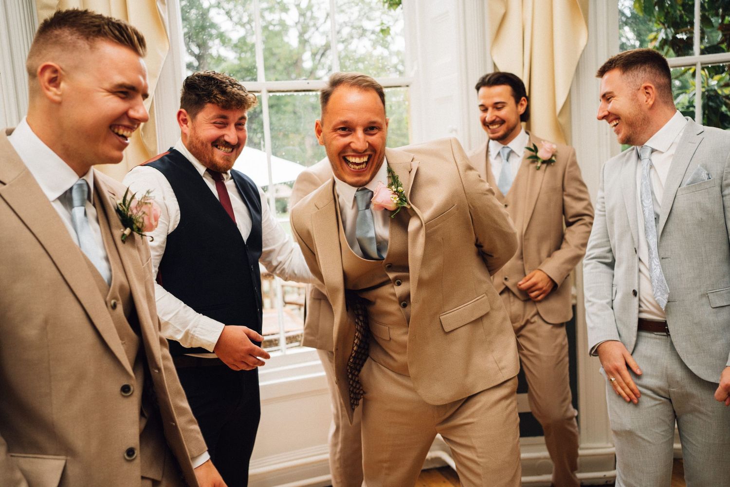 Wedding guests in tan suits share joyful laughter and conversation during a reception celebration.