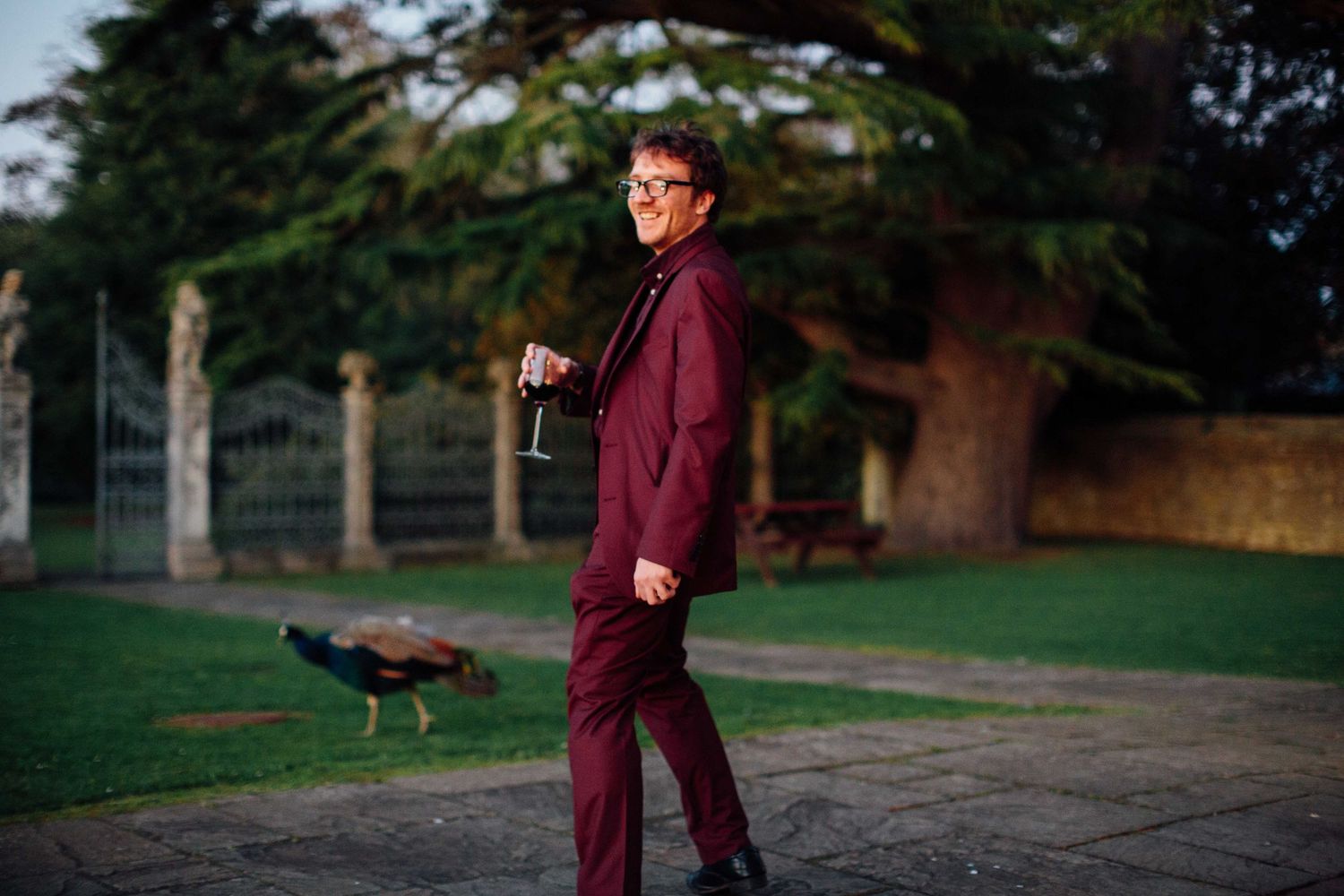 A person in burgundy attire poses with a bird of prey perched on their gloved hand in a park setting.