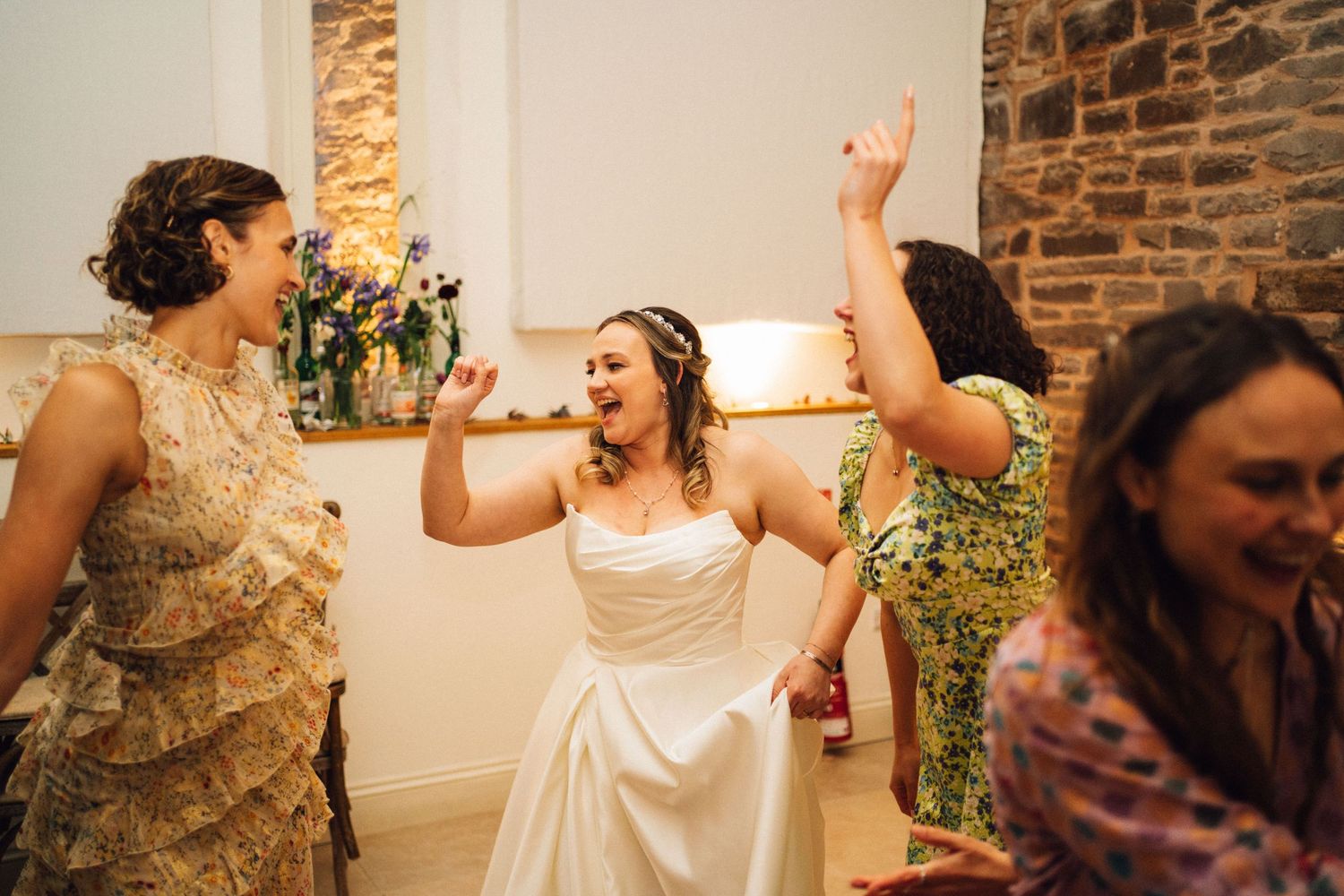 Wedding guests dance and celebrate together on a dance floor in a rustic stone-walled venue.