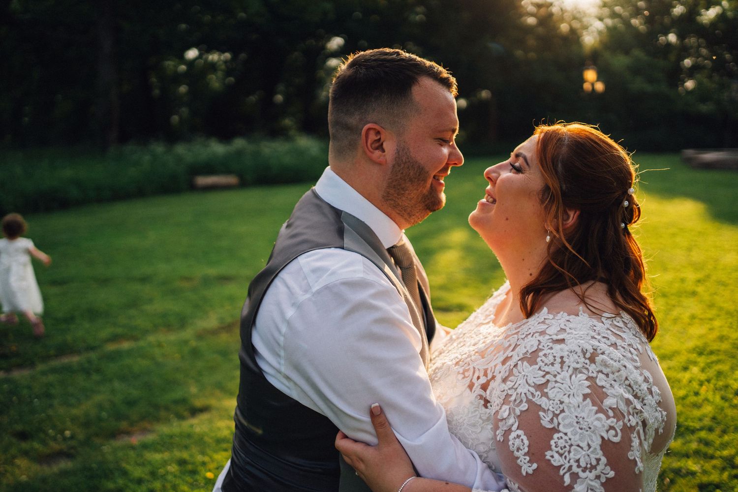 A couple shares an intimate laugh together during their sunset wedding photoshoot in a garden setting.