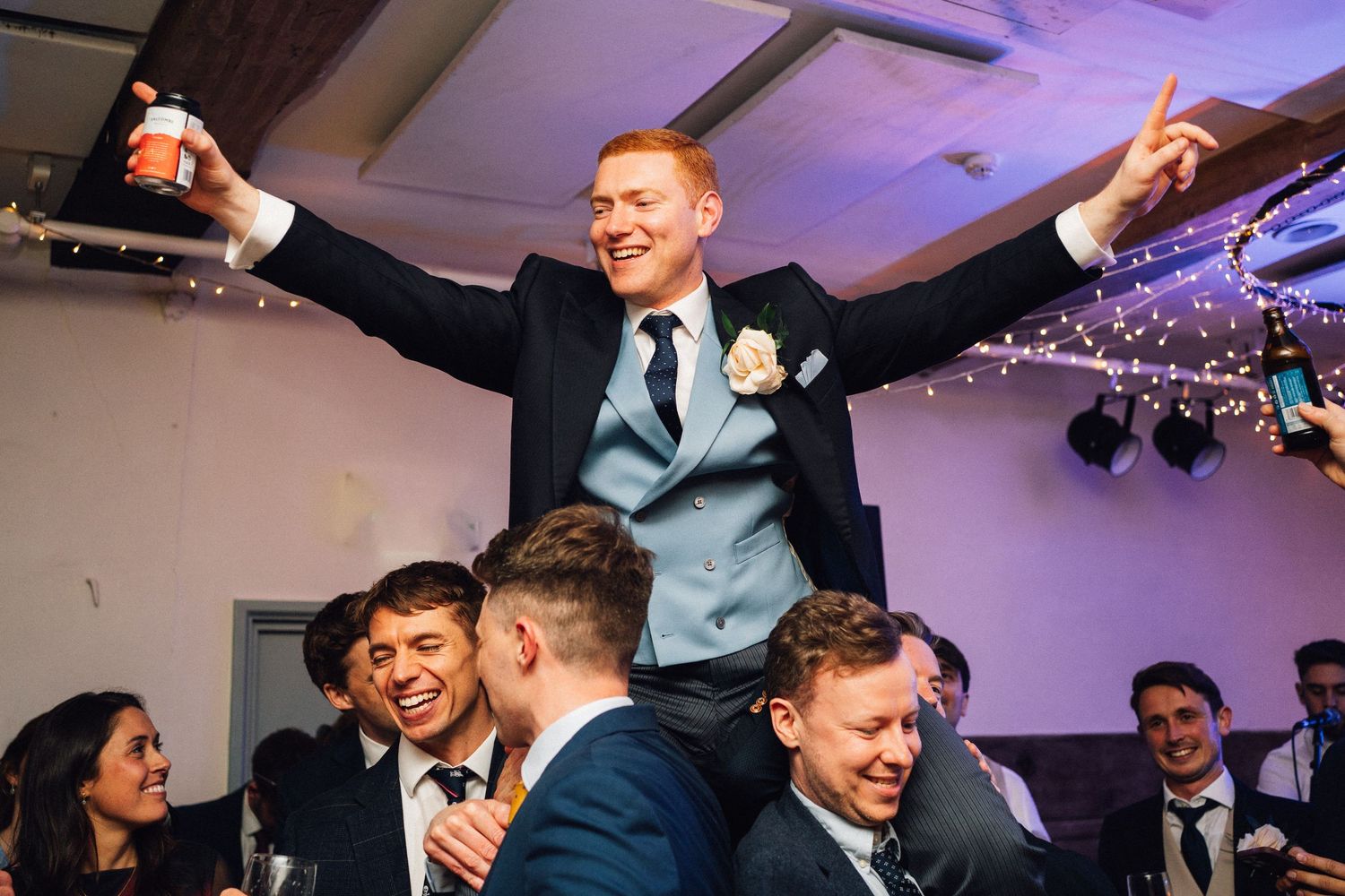 Energetic dance party at a wedding reception with purple ambient lighting and guests celebrating.