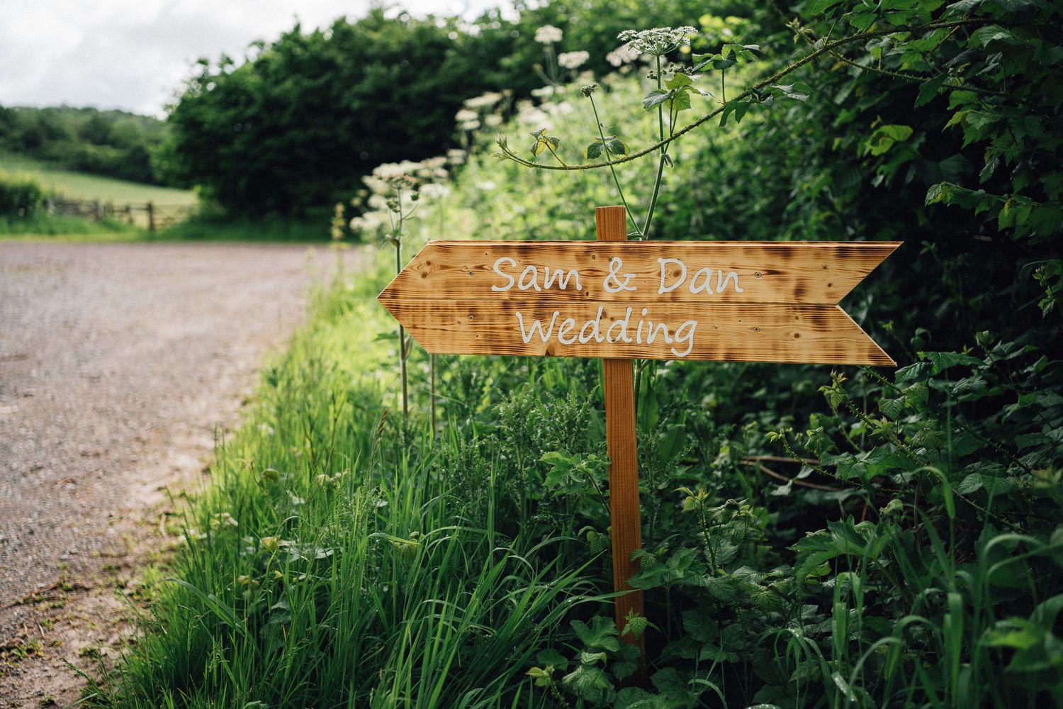 Rustic wooden directional sign along a country path with wildflowers and greenery.
