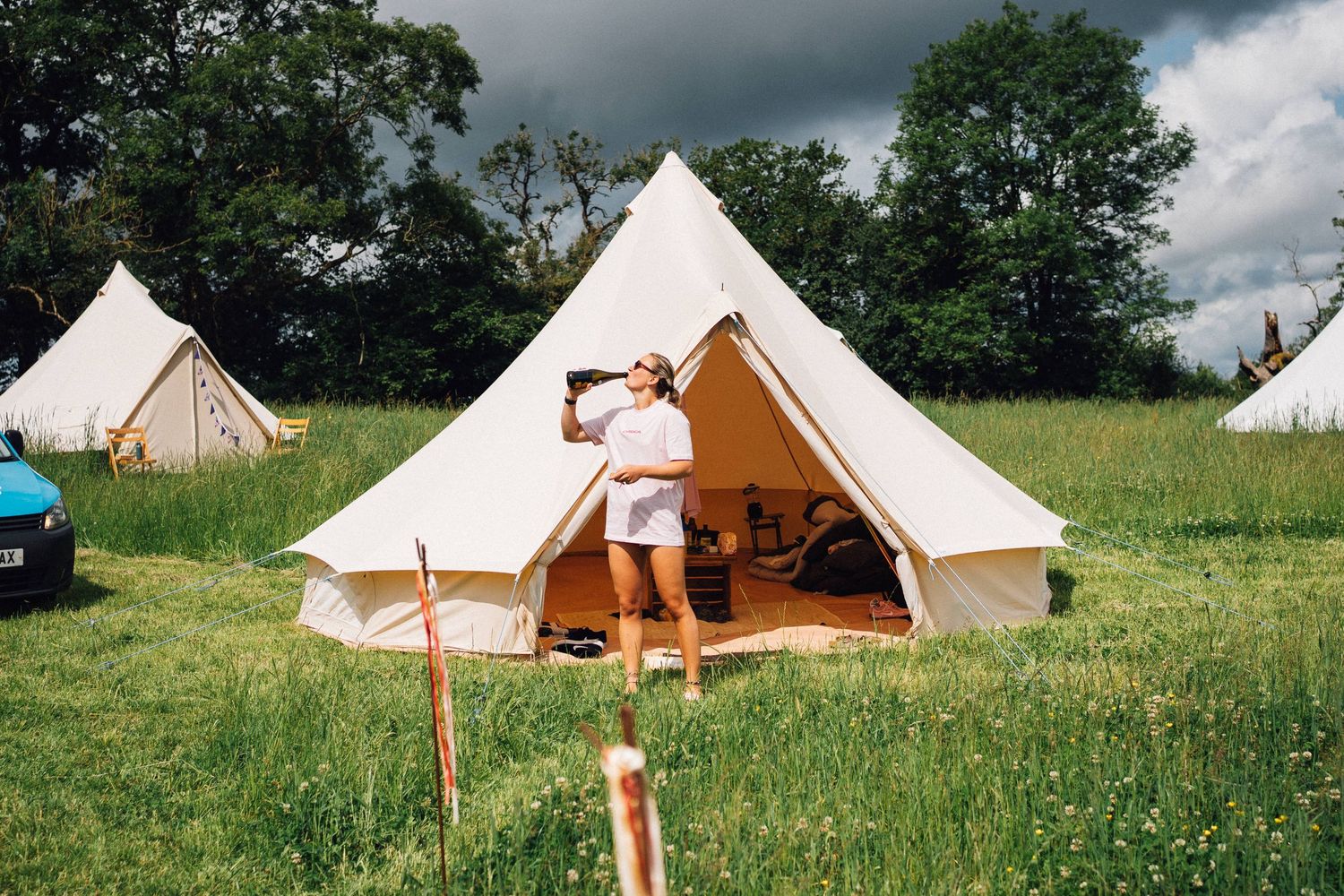 Luxury bell tents set up in a green field for glamping with cloudy skies in the background.